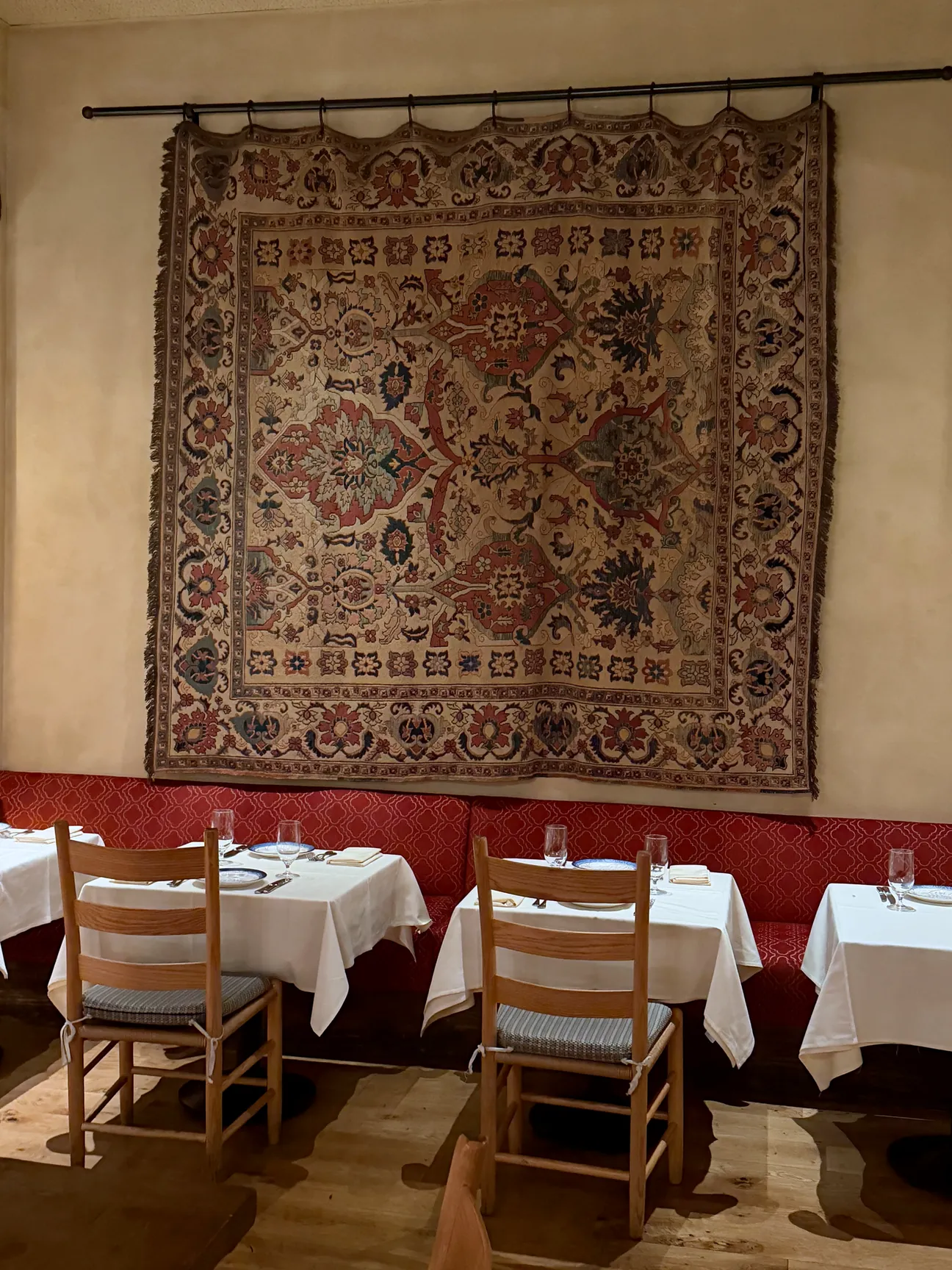 A dining room at Kokkari with an antique rug hung on the wall above a red banquette.