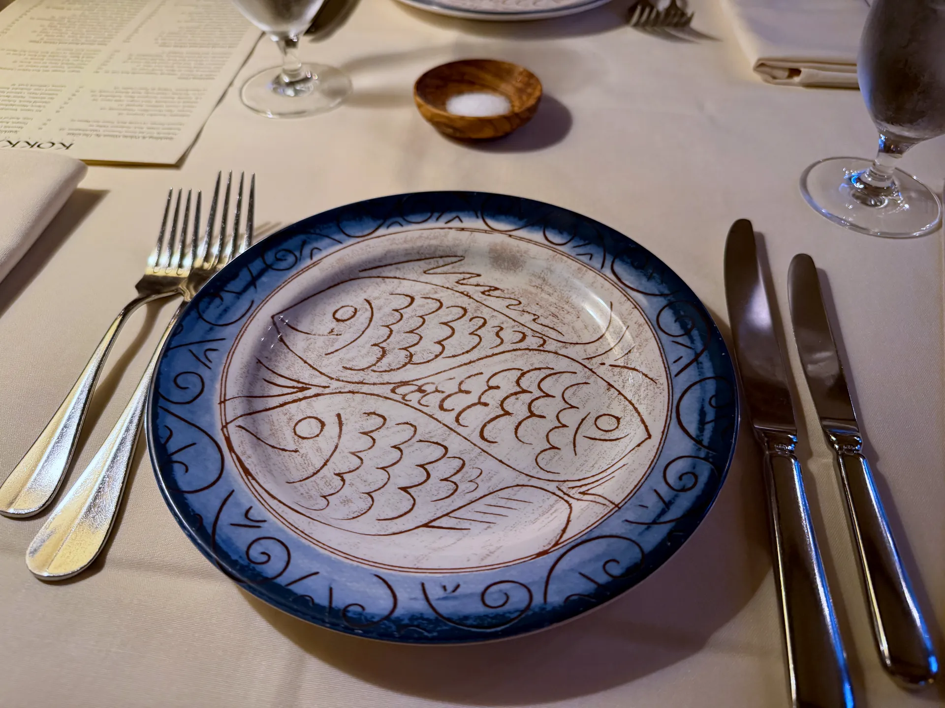 A blue and white plate painted with two fish at a set place, with cutlery and a salt dish.
