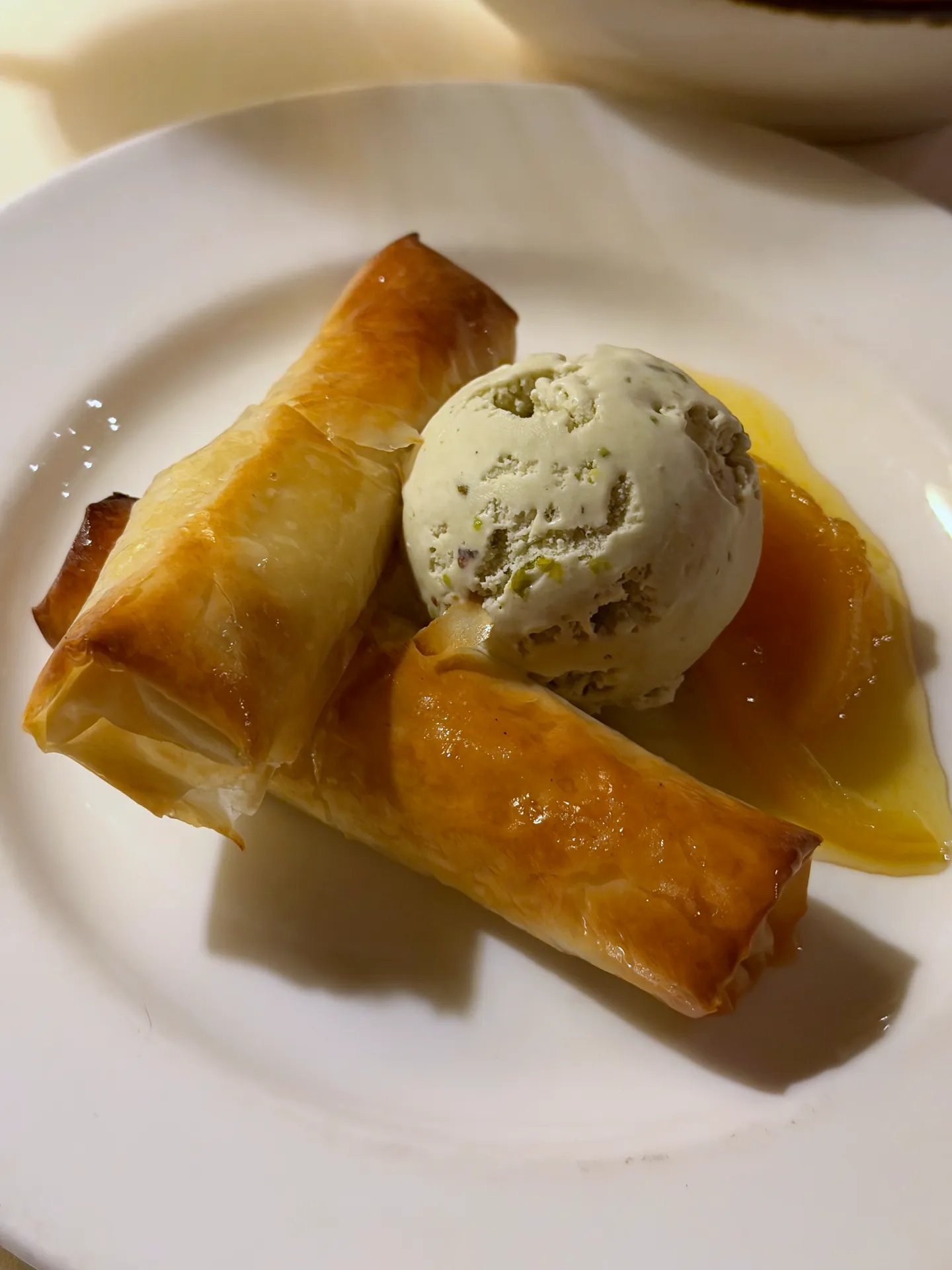 Two rolls of semolina custard in filo with a scoop of pistachio ice cream and syrup.