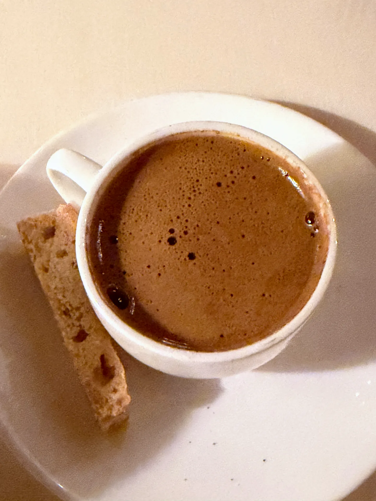 A cup of Greek coffee with foam on the surface and a biscuit on the saucer.