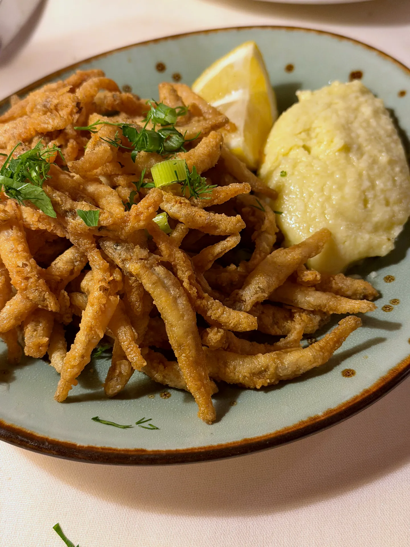 Crispy fried smelts on a green plate with a lemon wedge and a scoop of garlic potato skordalia.