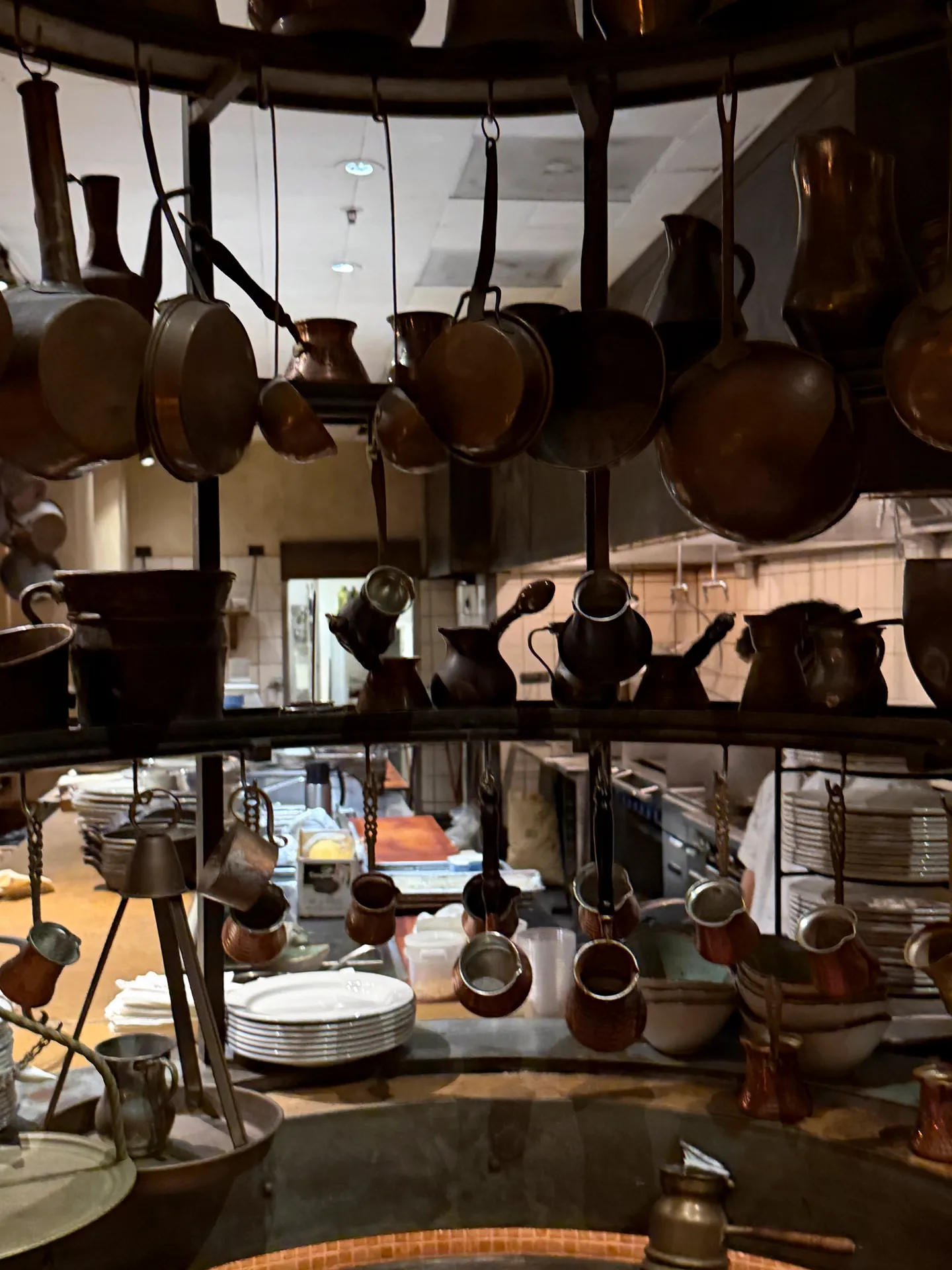Copper pots and pans hanging above the open kitchen at Kokkari, with plates stacked below.