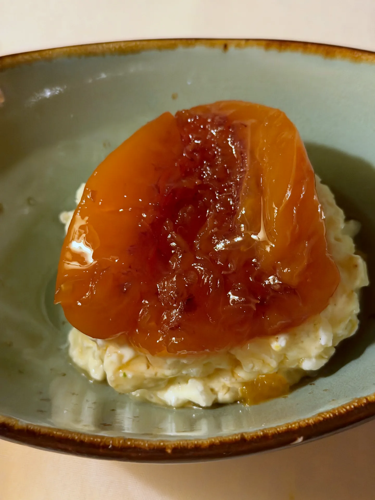 Rice pudding on a green plate topped with a honey roasted peach half.