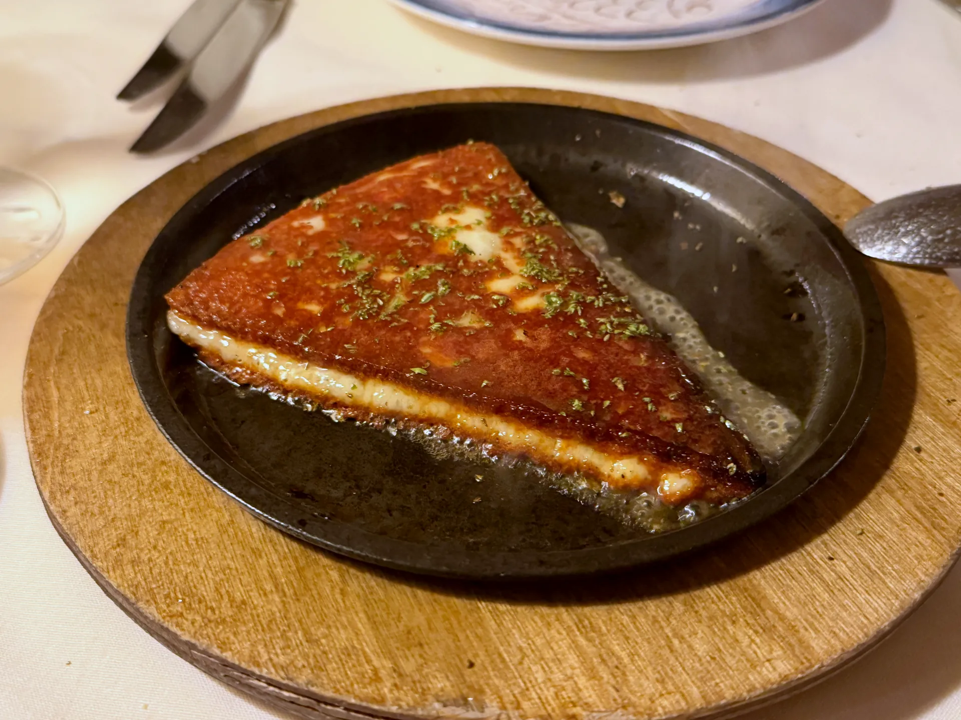 A wedge of pan fried Kefalotyri cheese in a small skillet on a wooden board.