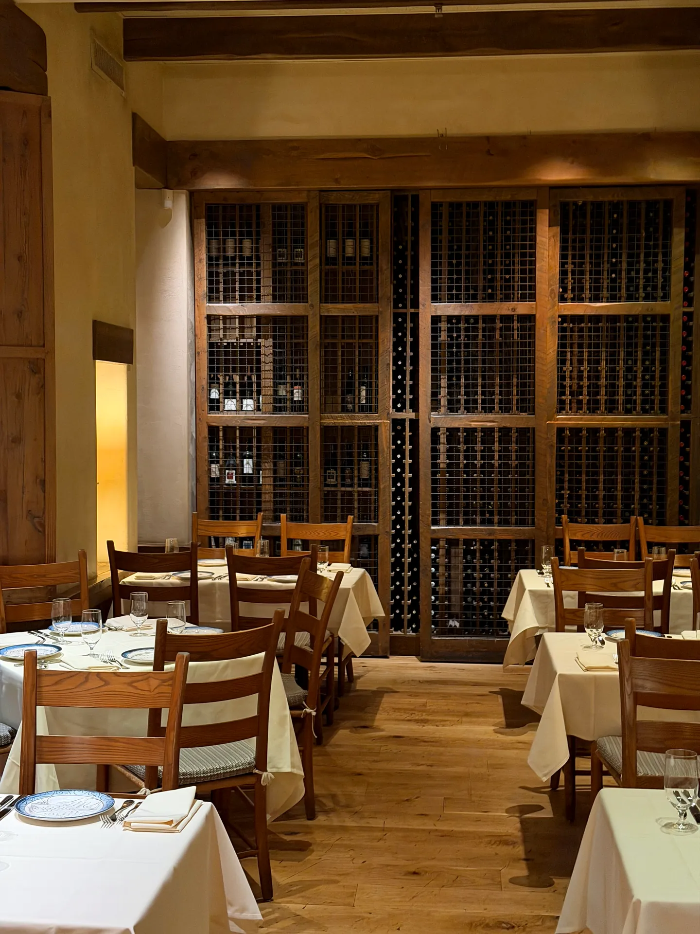 A dining room at Kokkari lined floor to ceiling with wine racks behind set tables.