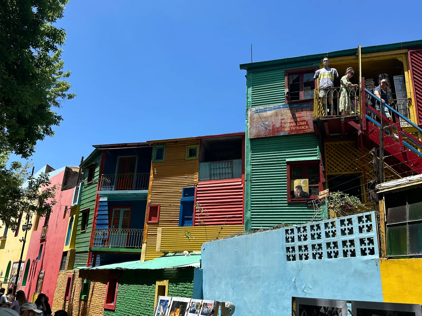 Stacked painted balconies with figures leaning out at Caminito, La Boca.