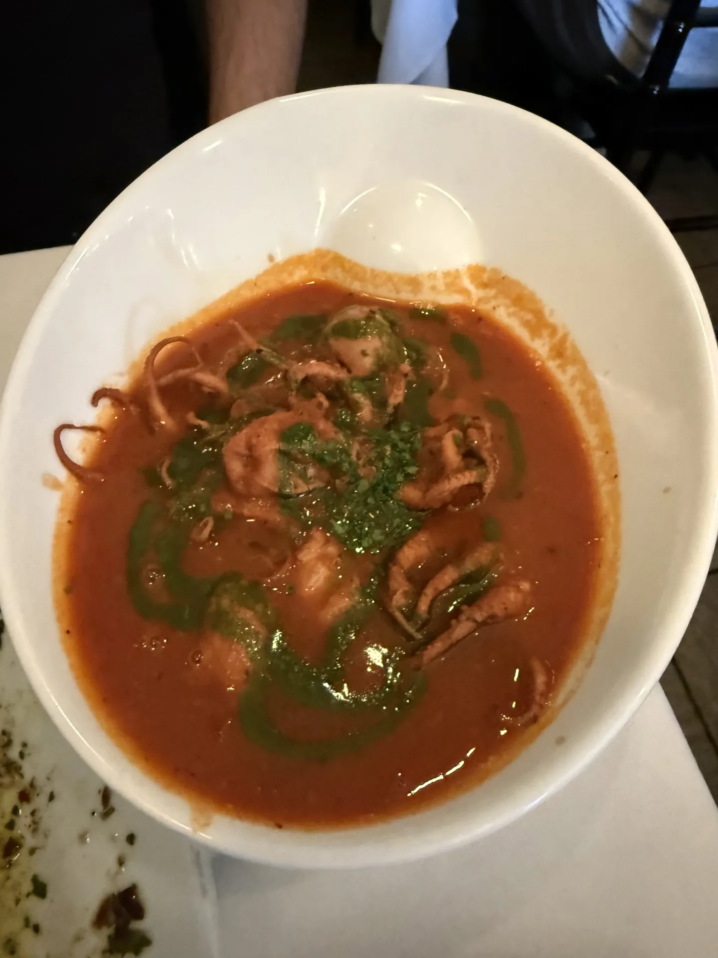 Baby octopus stewed in tomato sauce with herb oil in a white bowl.