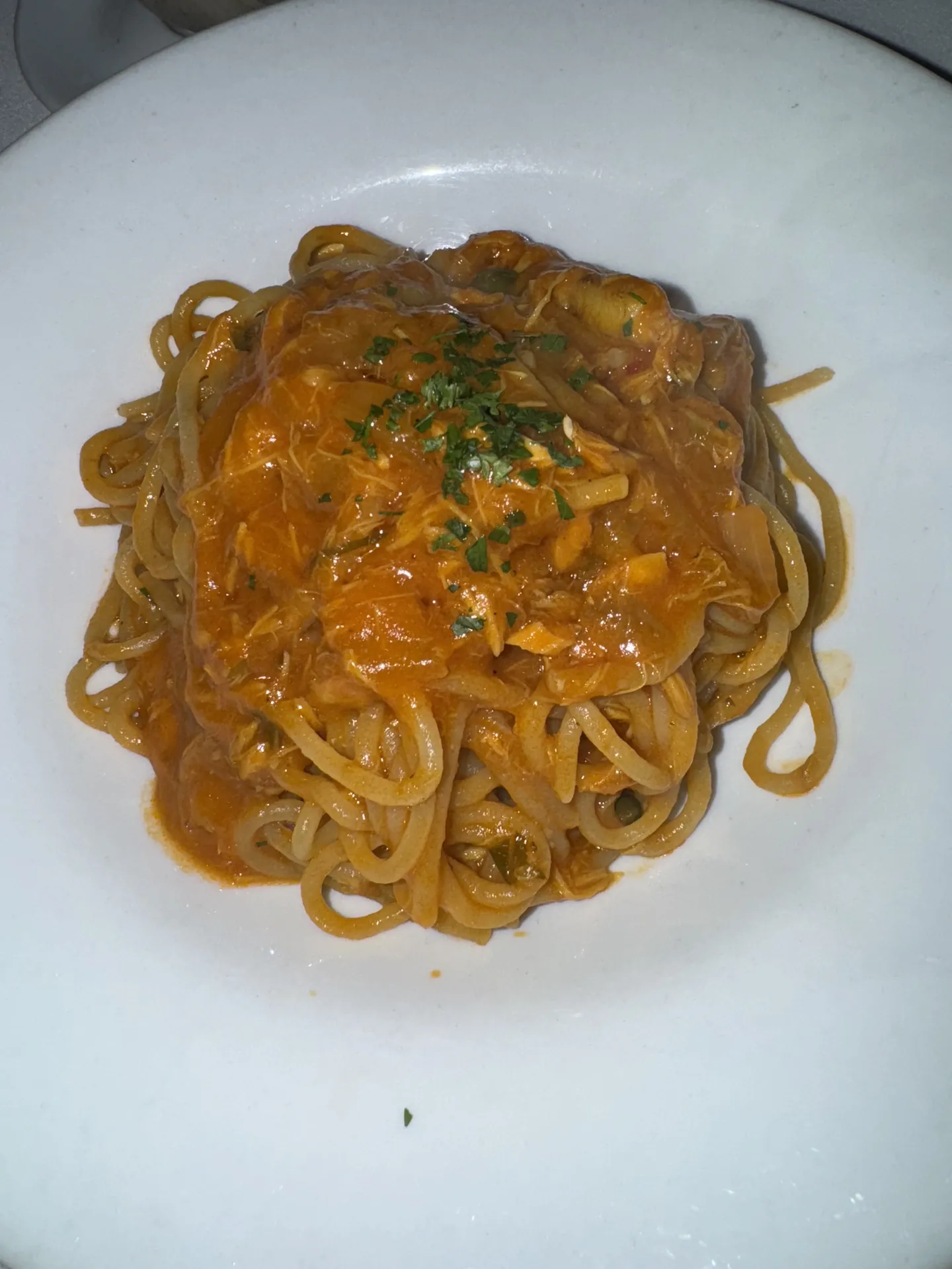 Long pasta in a creamy tomato and crab sauce on a white plate.