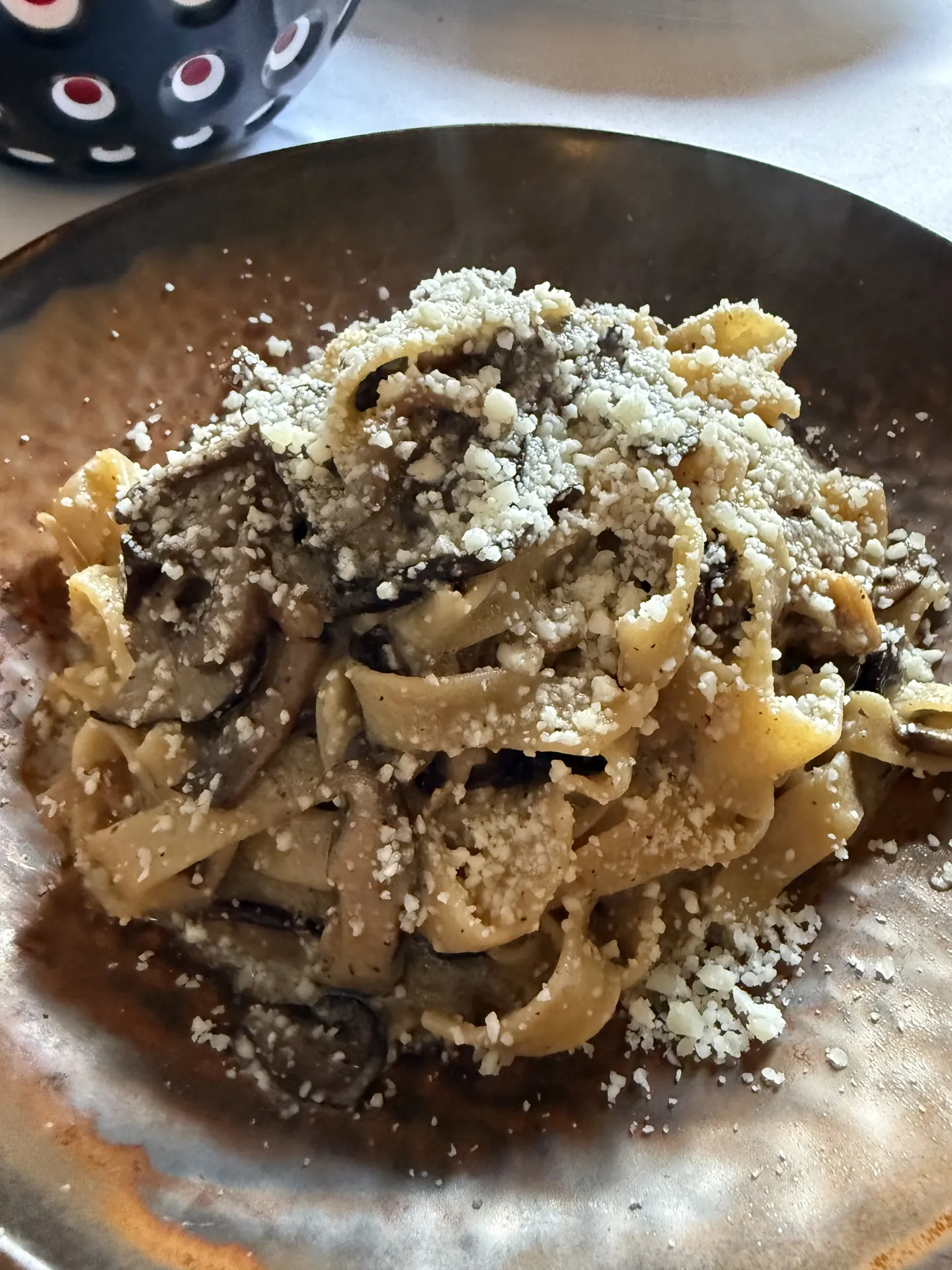 Tagliatelle with mushrooms and grated cheese in a dark bowl.