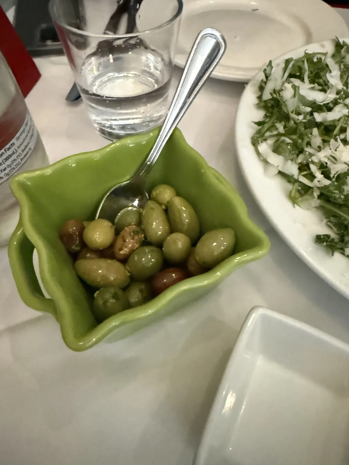 A dish of marinated green olives beside a plate of arugula.