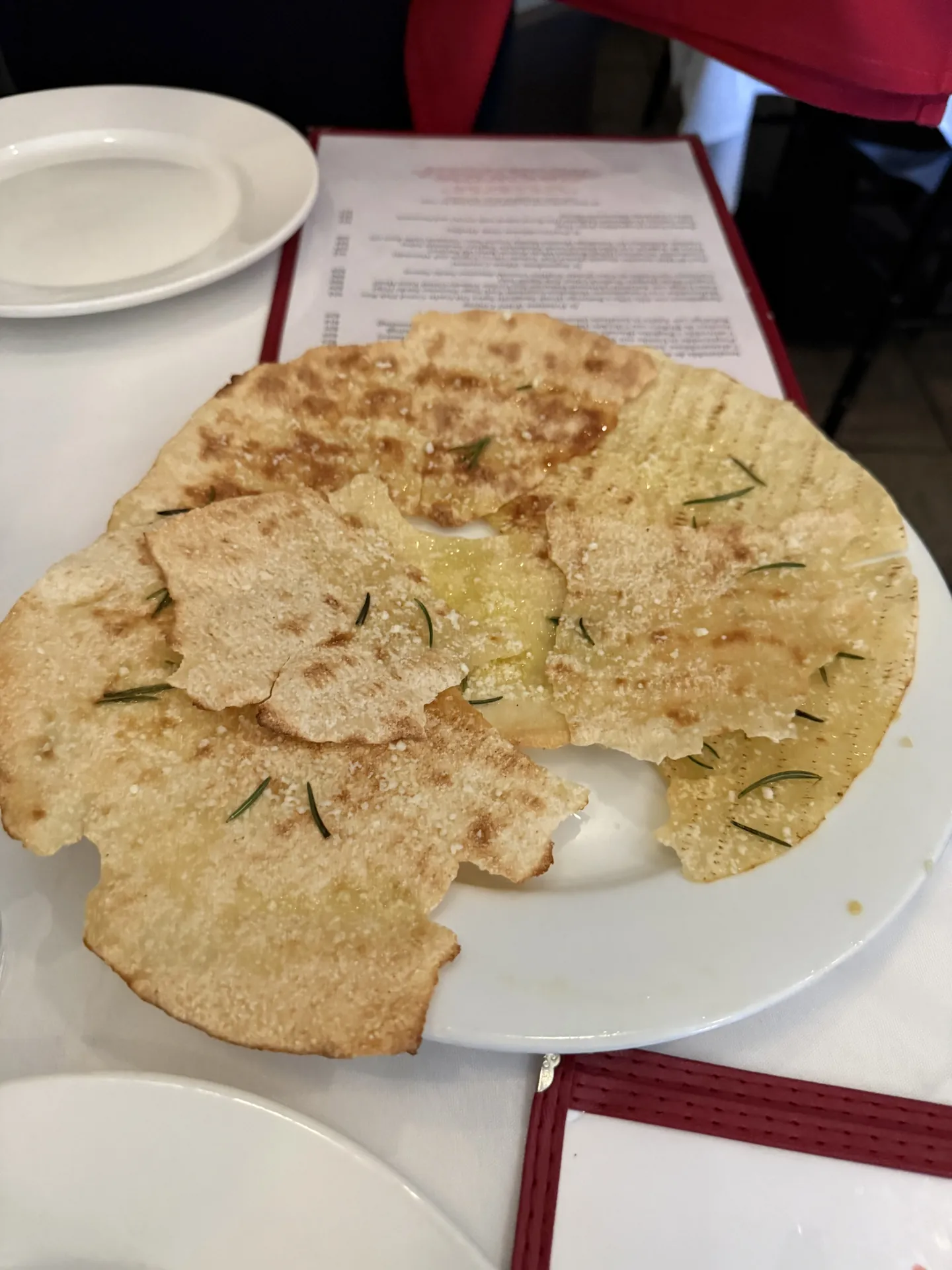 Pani guttiau, a thin crisp Sardinian flatbread with rosemary, on a white plate.