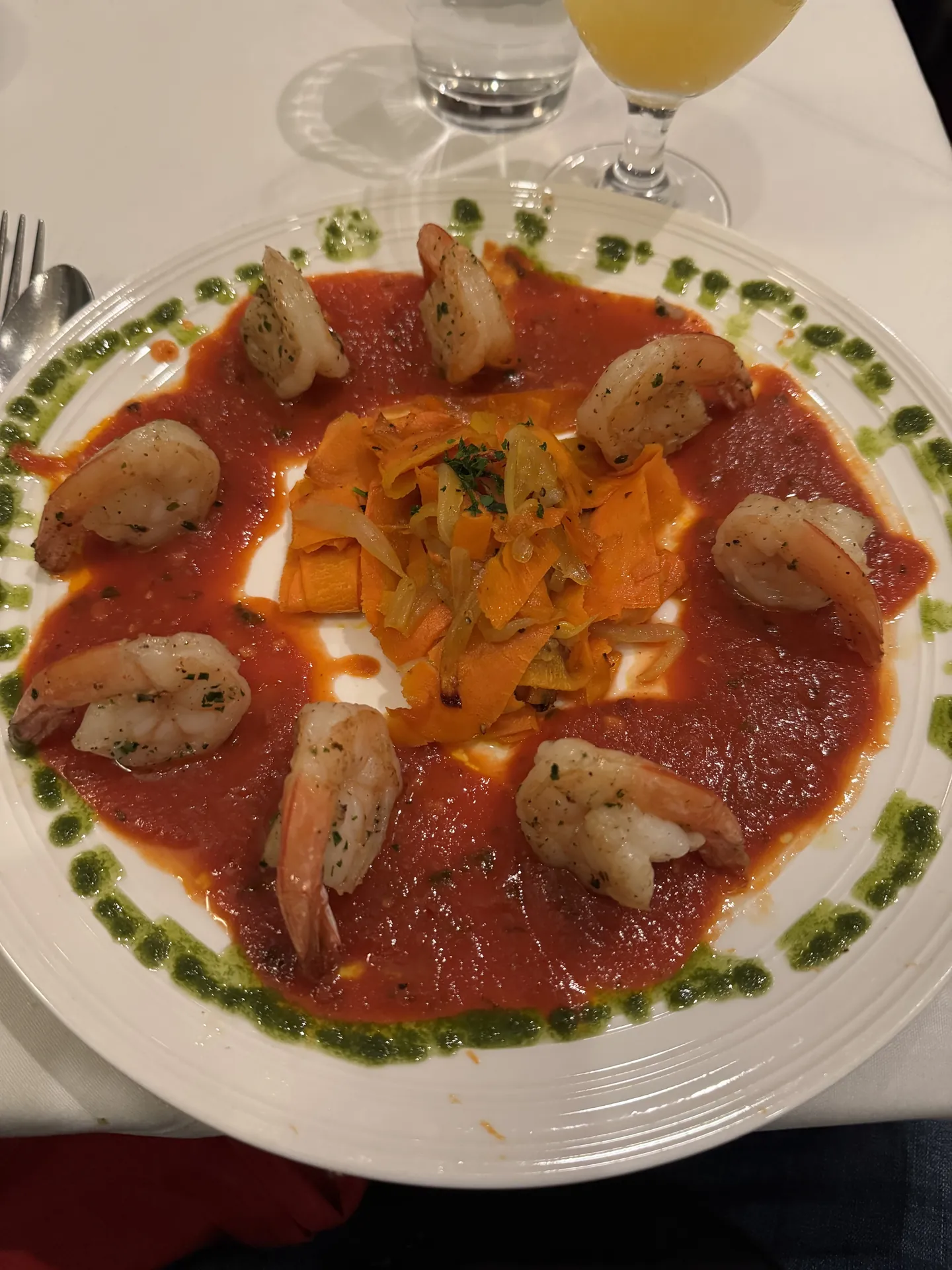Roasted prawns arranged around a tomato coulis with fennel and herb oil on a white plate.