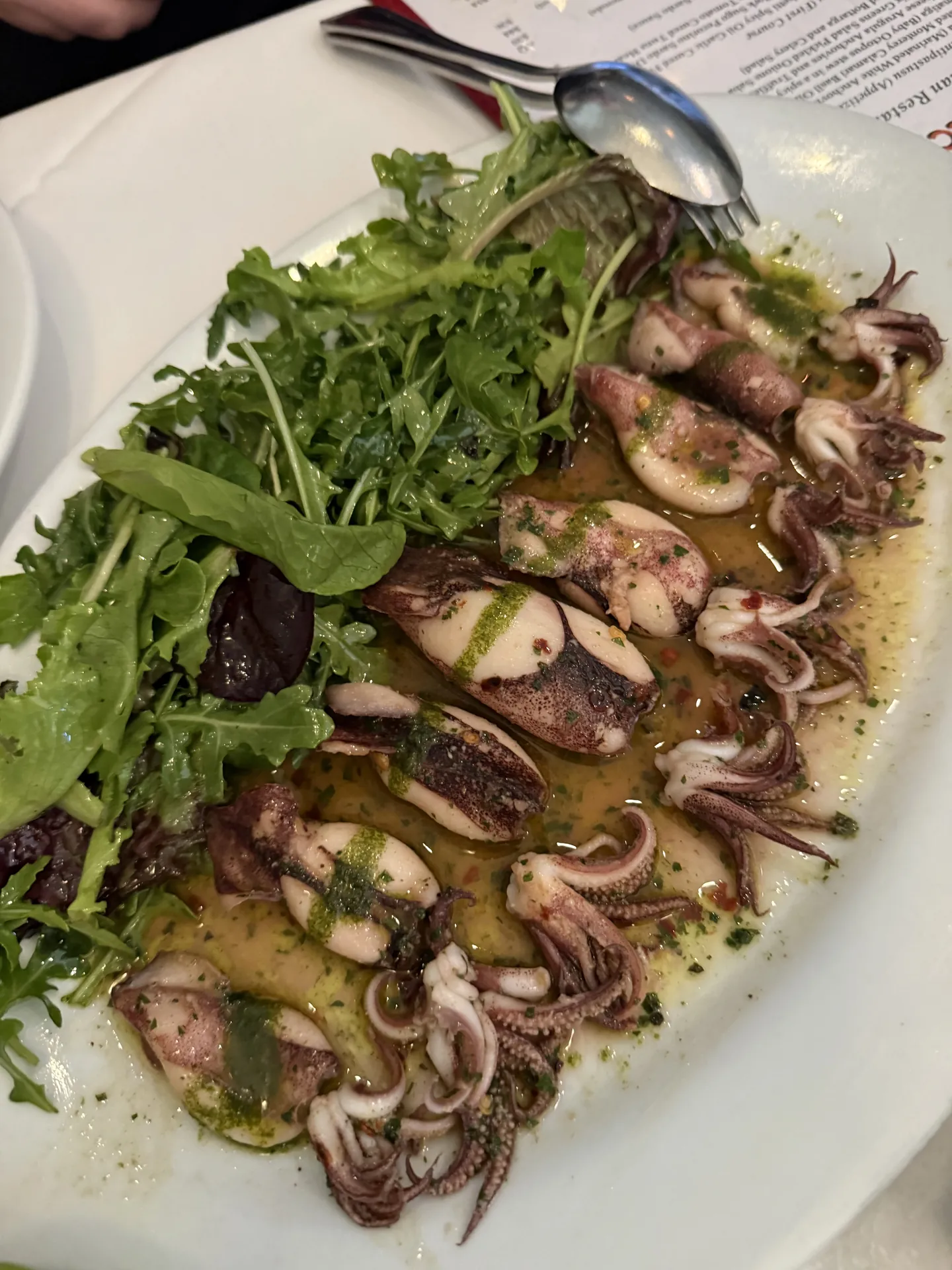 Roasted Monterey calamari with basil oil over mixed greens on an oval plate.