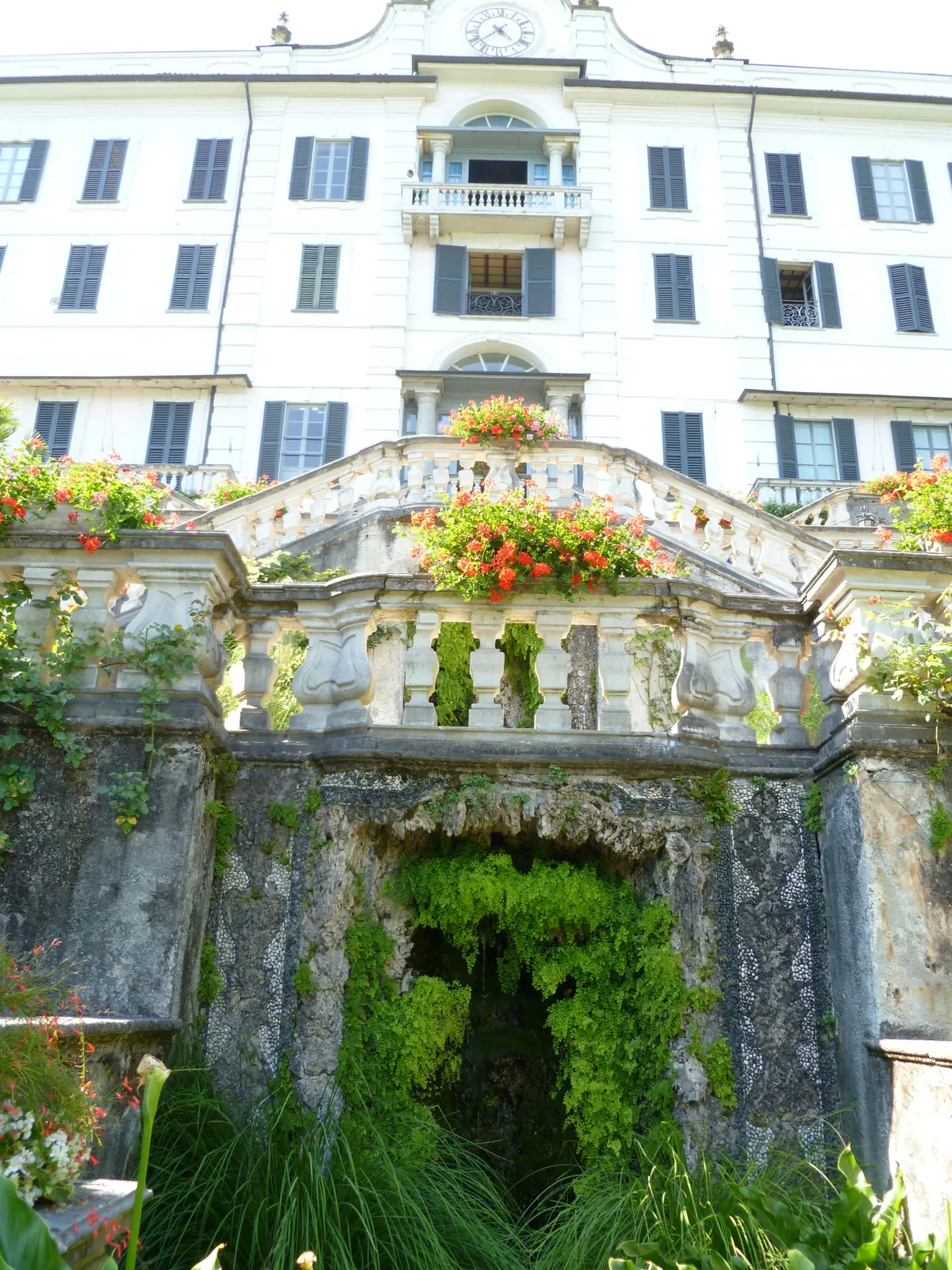 A rustic grotto set into the terrace wall at Villa Carlotta, framed by red geraniums.