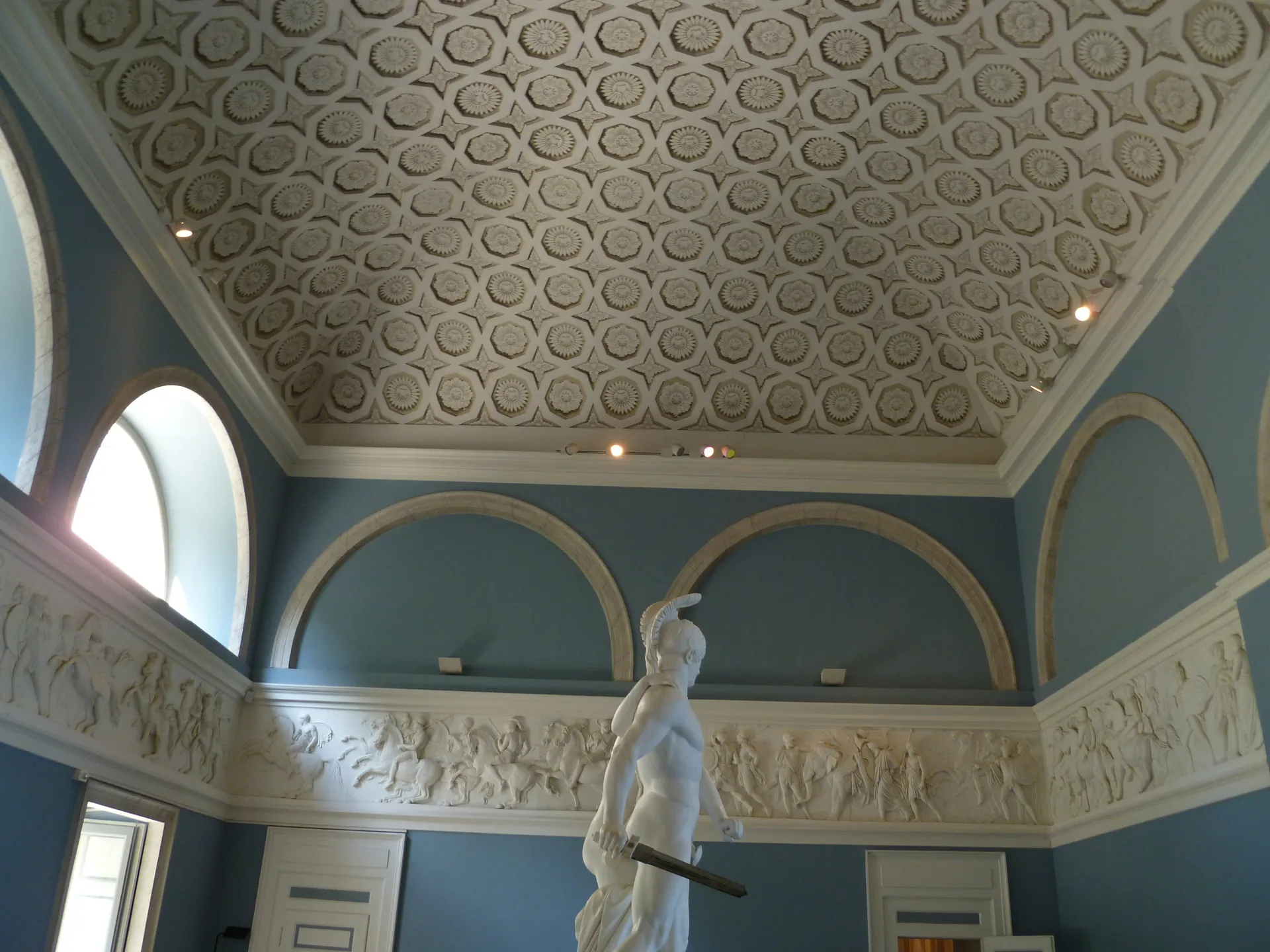 A marble statue and a long relief frieze on the blue walls of the Villa Carlotta gallery.