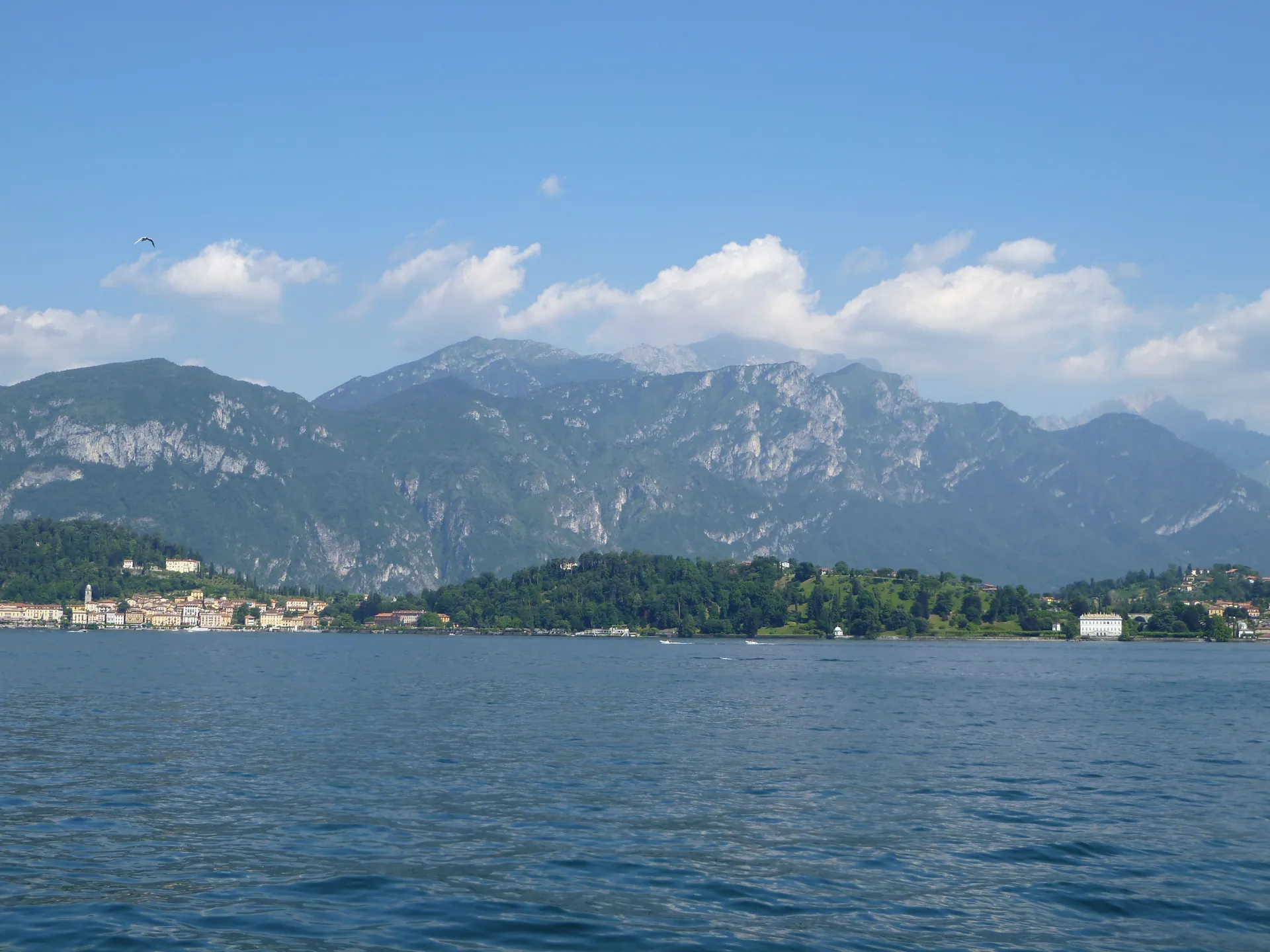 The wooded Bellagio promontory and mountains seen across Lake Como from a ferry deck.