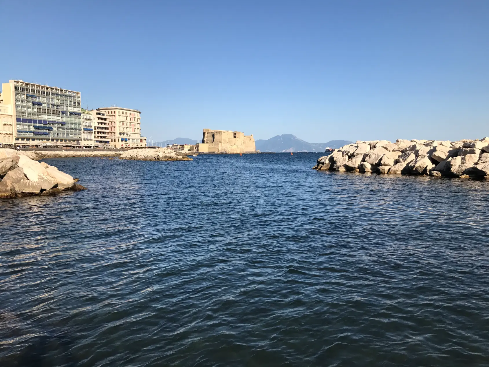 Castel dell'Ovo seen from across the inlet with modern buildings on the Naples shore.