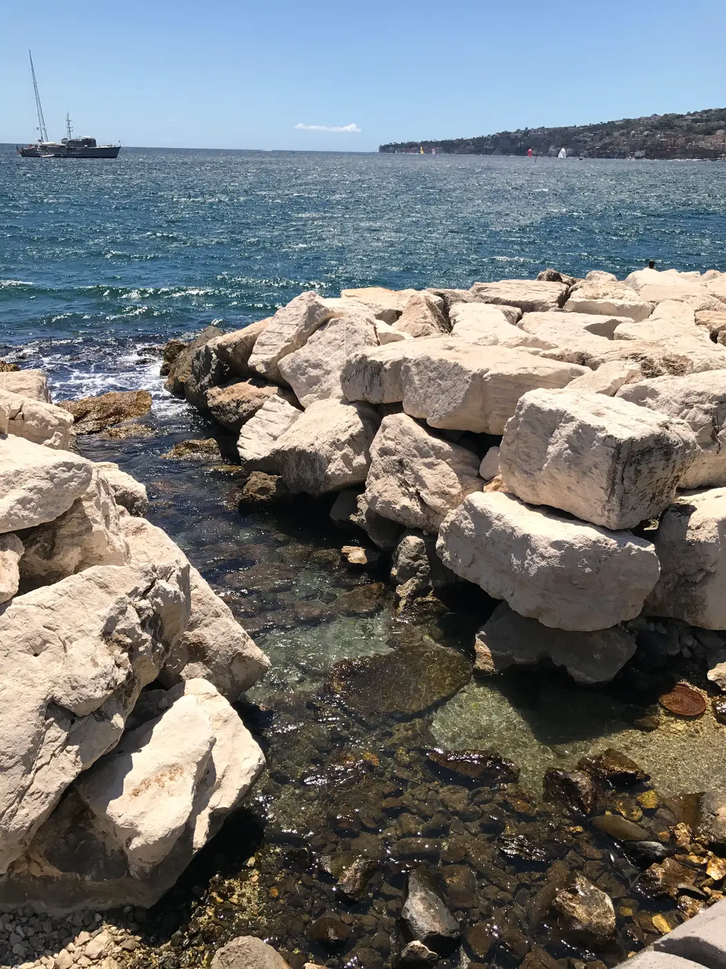 Clear shallow water between the quarried stone blocks of the Naples sea wall.