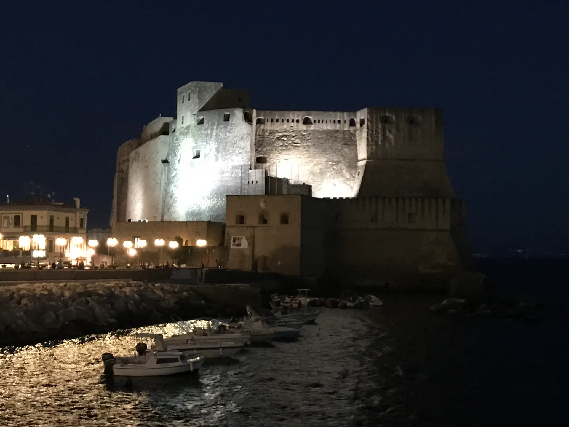 Castel dell'Ovo floodlit at night reflected across the water in Naples.