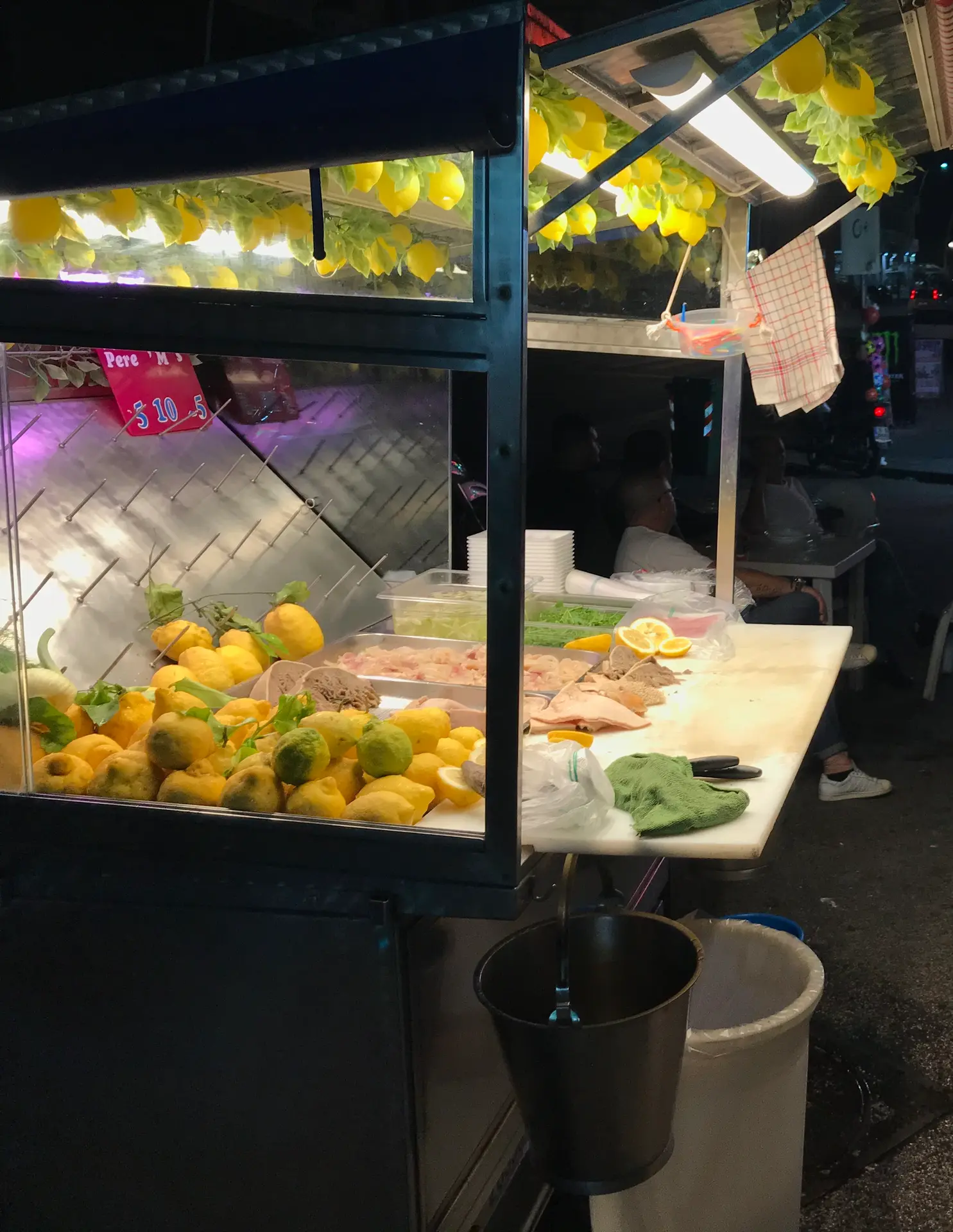 A lemon granita cart lit at night on the Naples seafront with a taralli stand behind.