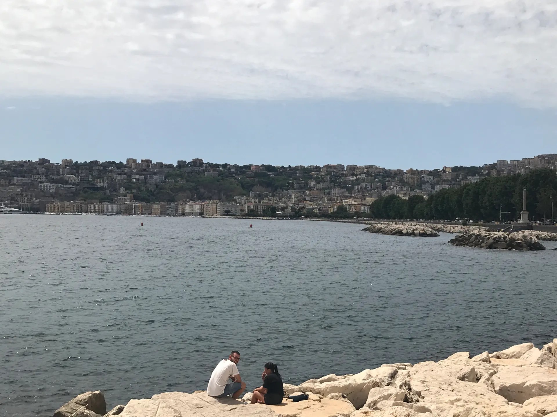 Two people sitting on the rock breakwater on the Naples seafront.