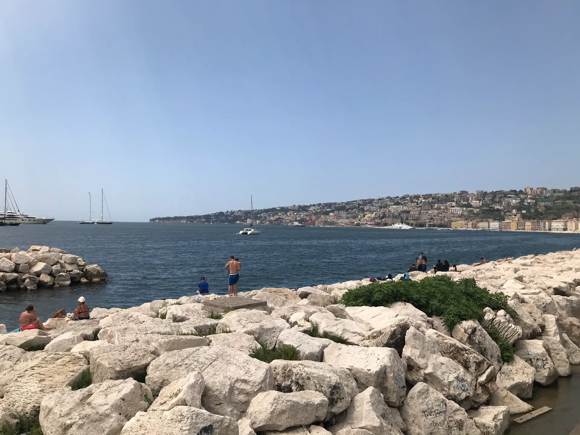 Sunbathers lying on the flat stone blocks of the Lungomare breakwater in Naples.