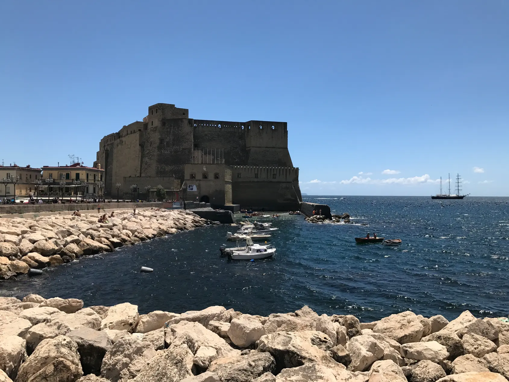 Castel dell'Ovo with a tall ship anchored offshore in the Bay of Naples.