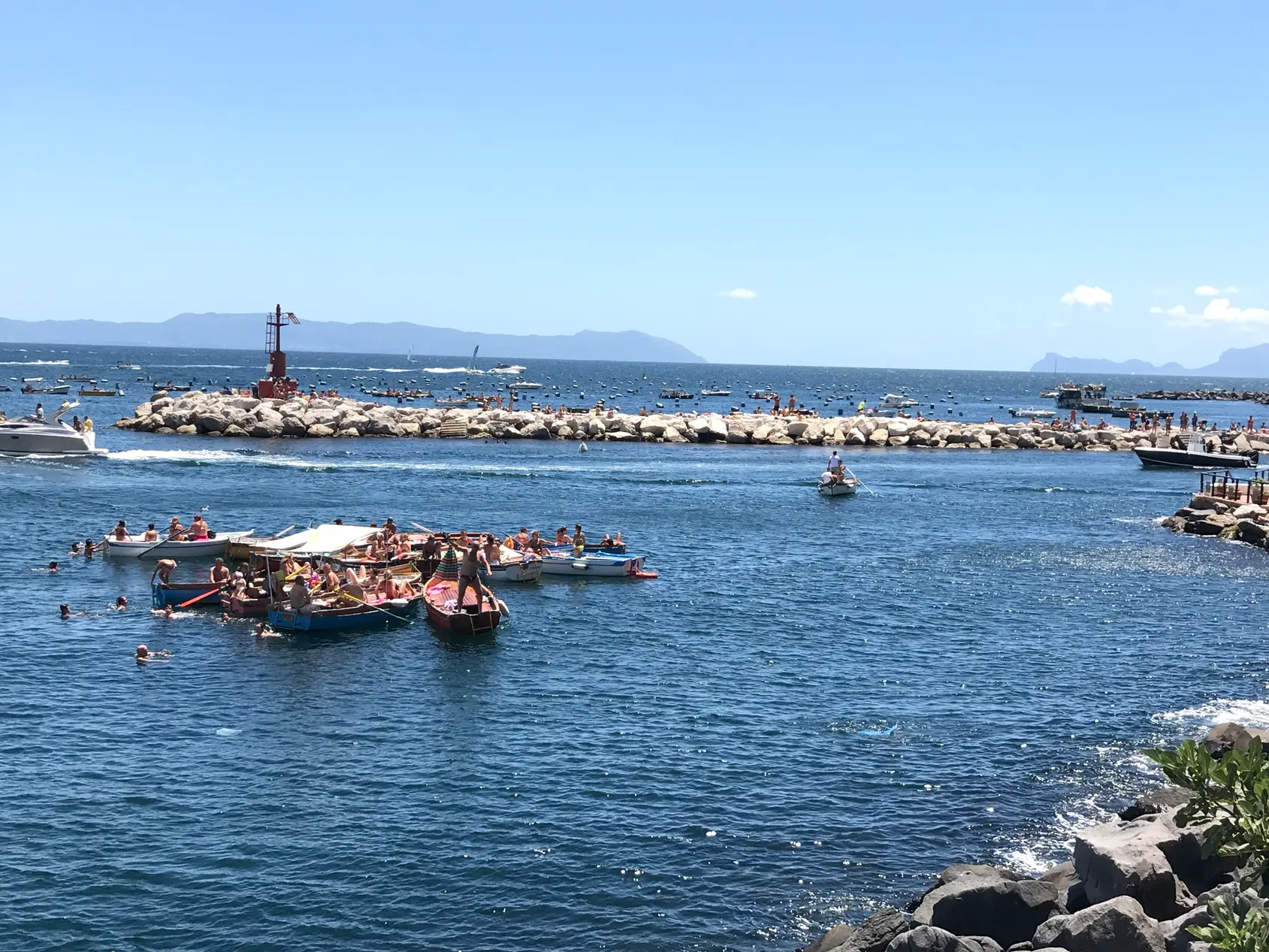 A crowded floating swimming platform moored off the Naples seafront breakwater.