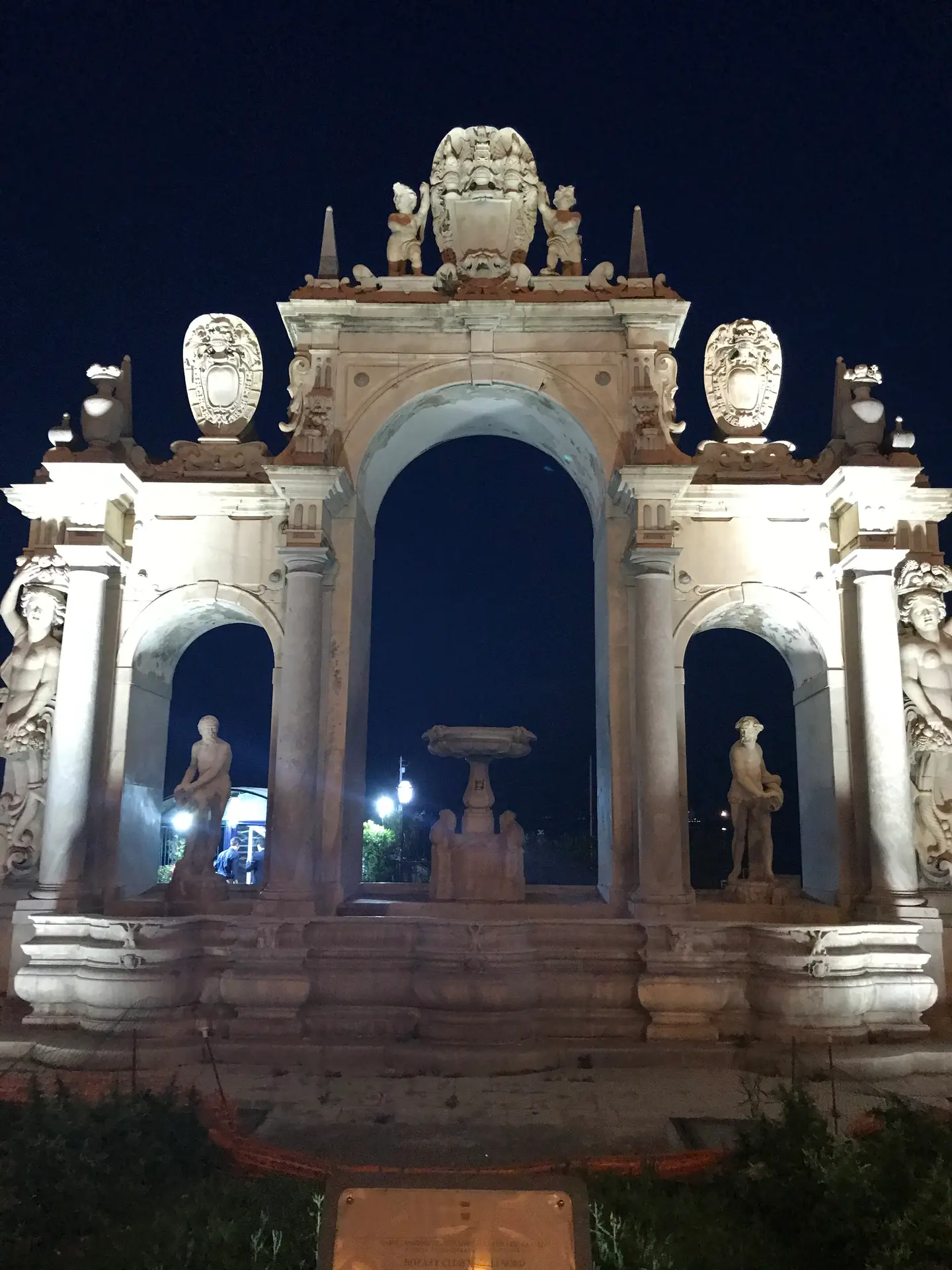 The Fontana dell'Immacolatella floodlit at dusk on the Naples seafront.