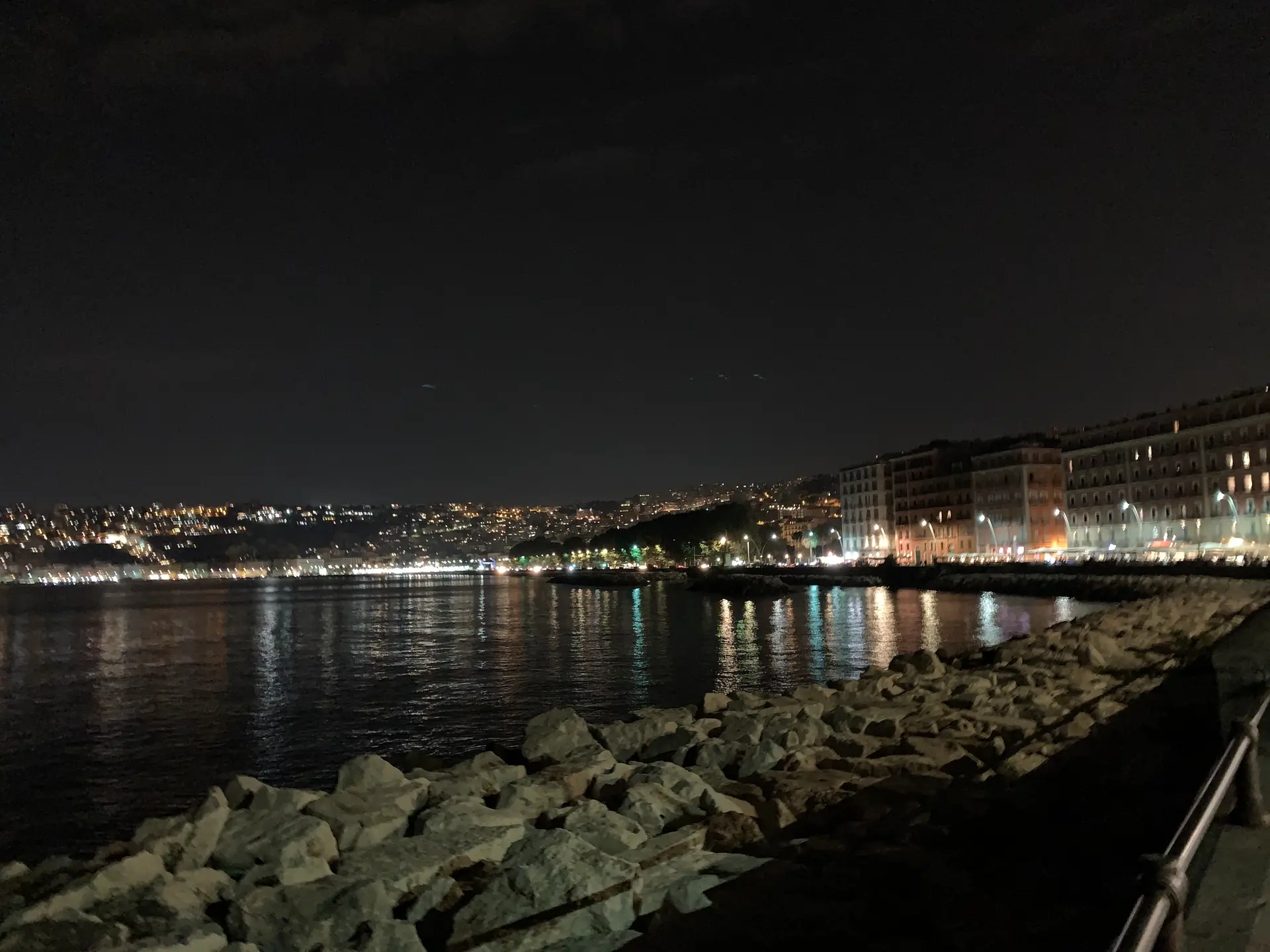 The lit hotel fronts and terraces of the Naples seafront seen at night.