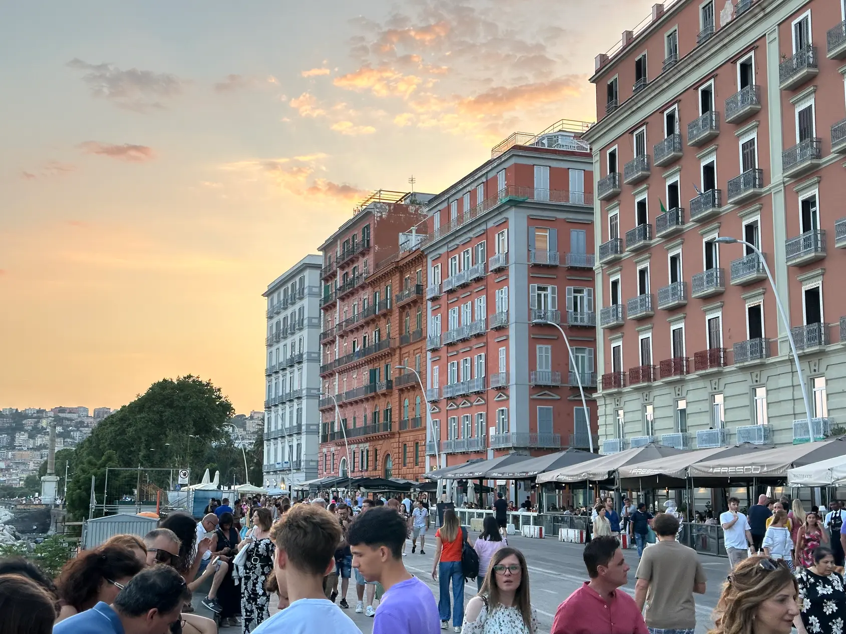 Crowds on Via Partenope in Naples at sunset with the buildings lit orange.