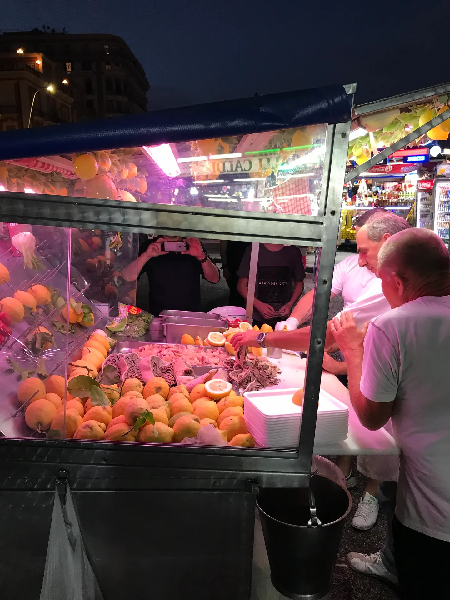 A lit street cart on the Naples seafront selling lemon granita and boiled seafood at night.