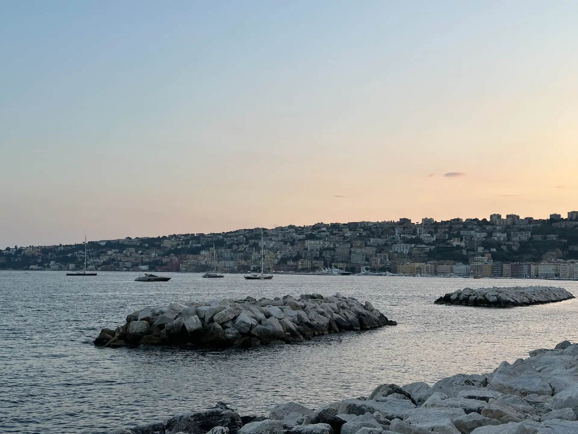 The hill of Posillipo at sunset seen across the breakwaters from the Naples seafront.