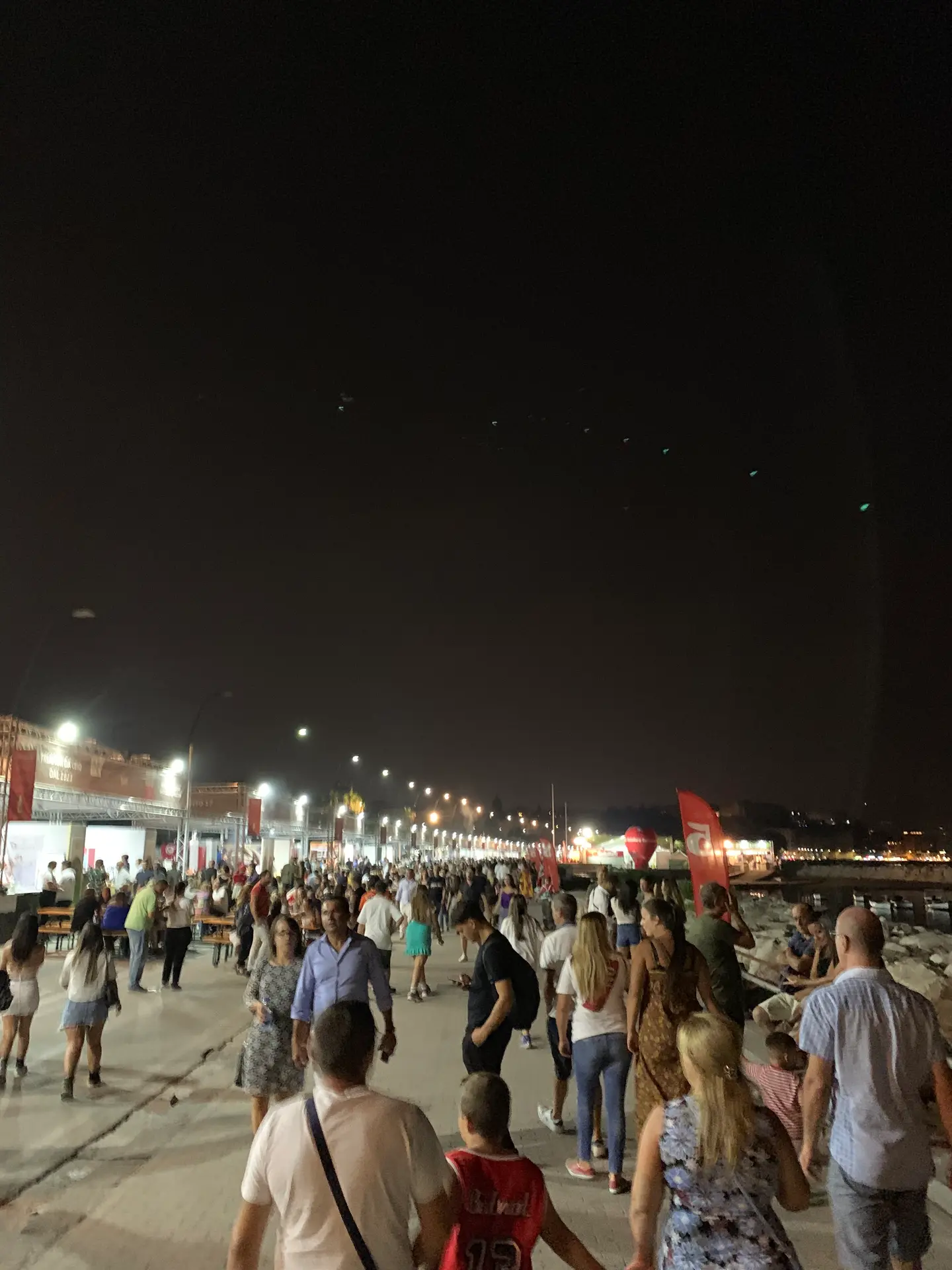 Crowds walking the Naples seafront promenade at night under the street lights.