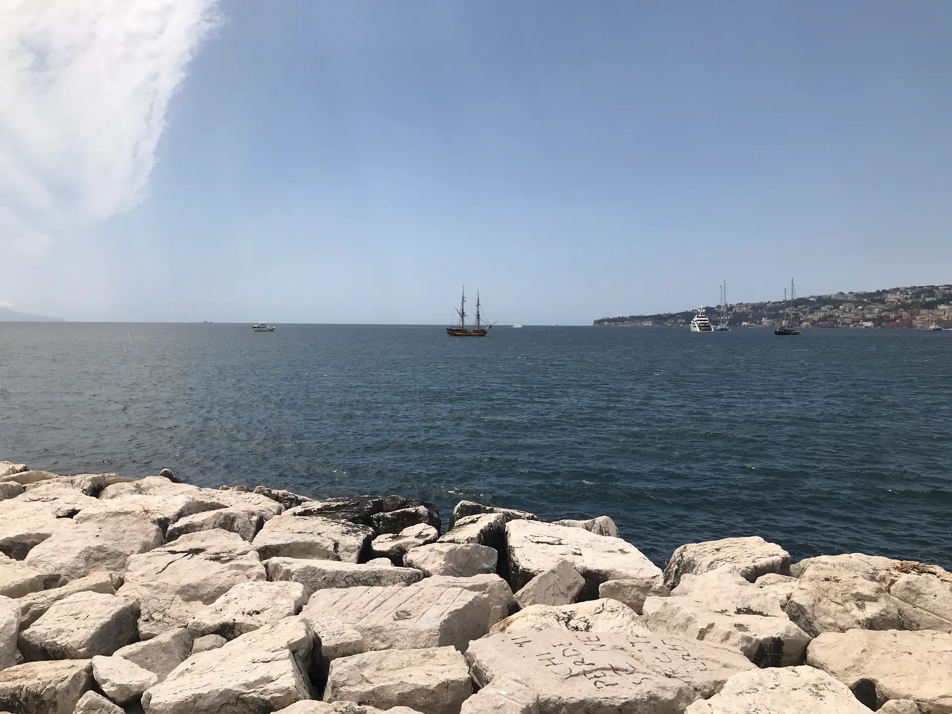 A tall sailing ship anchored off the rock breakwater on the Naples seafront.