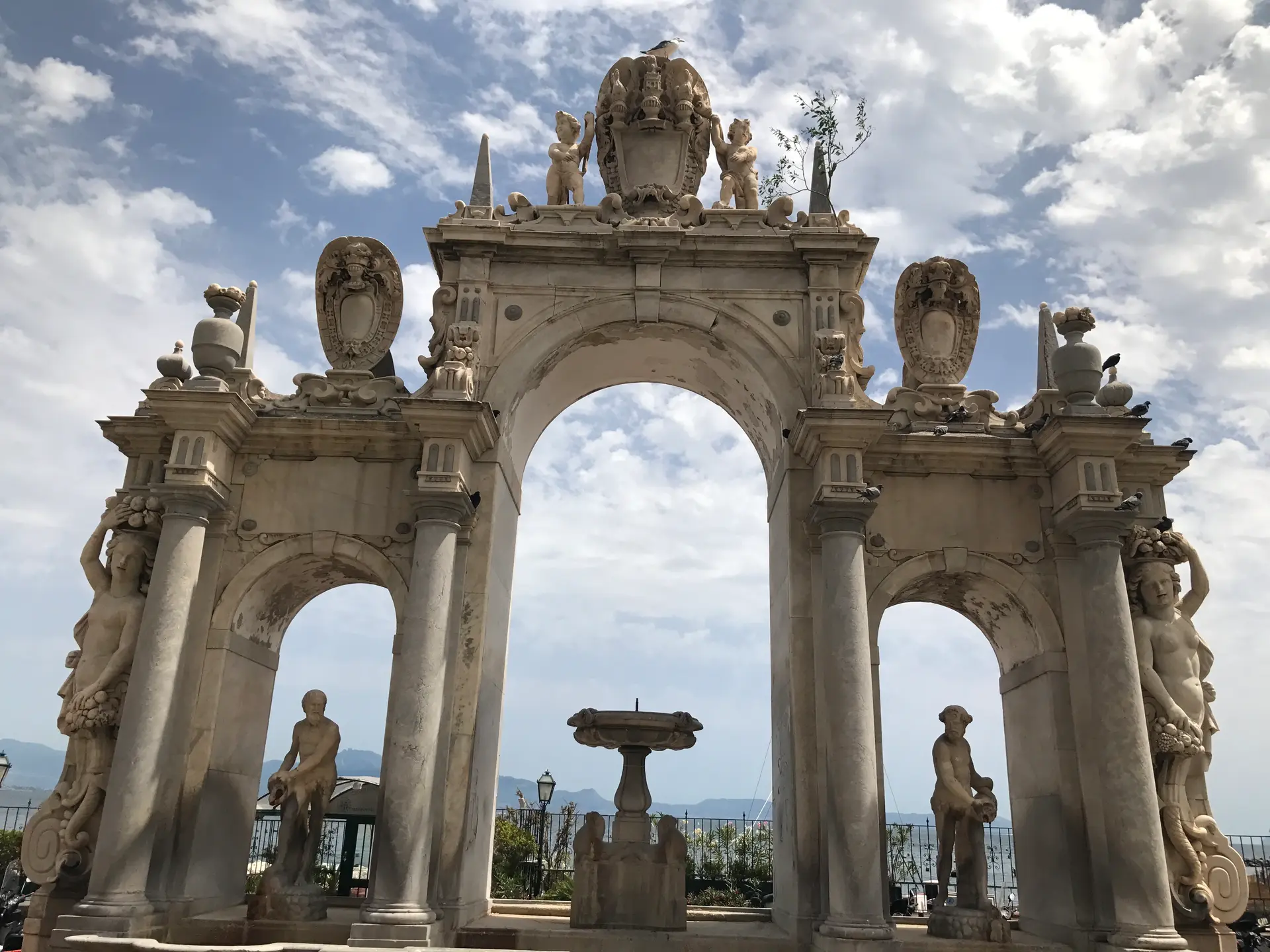 The three arches of the Fontana dell'Immacolatella seen from below against the sky.
