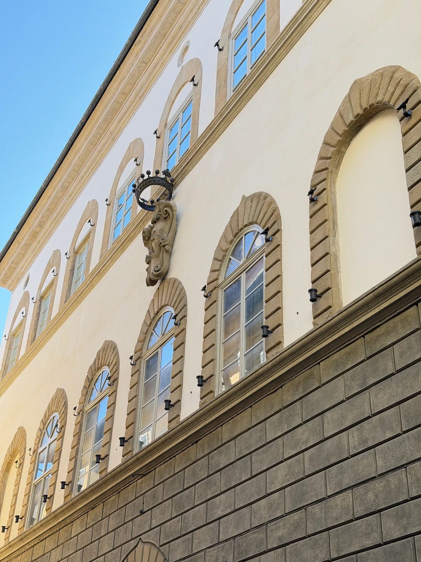 A row of arched windows along a rendered palace front, an iron lamp bracket between them.