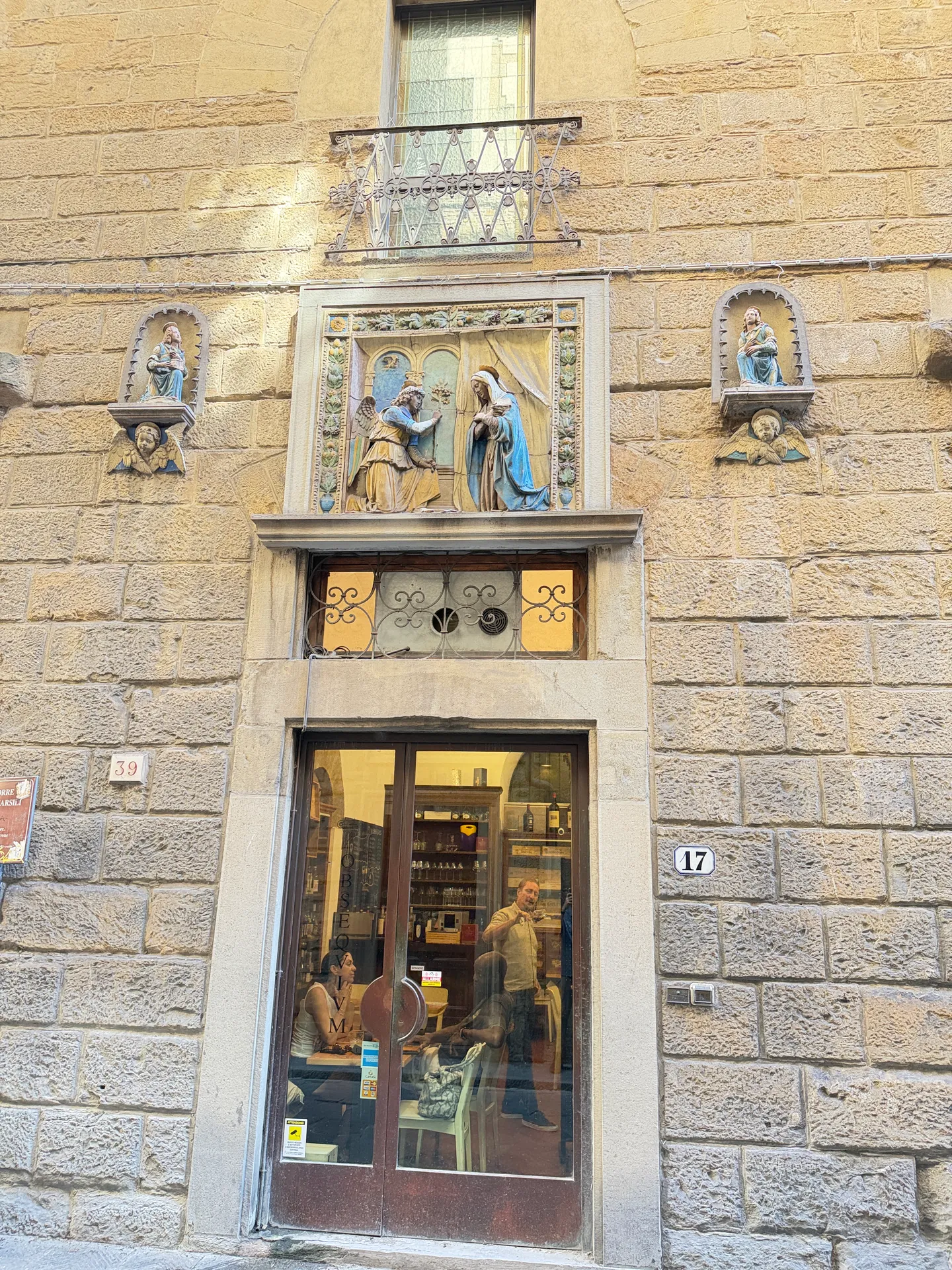 Glazed terracotta figures set in niches above a shopfront, with a coloured panel between them.
