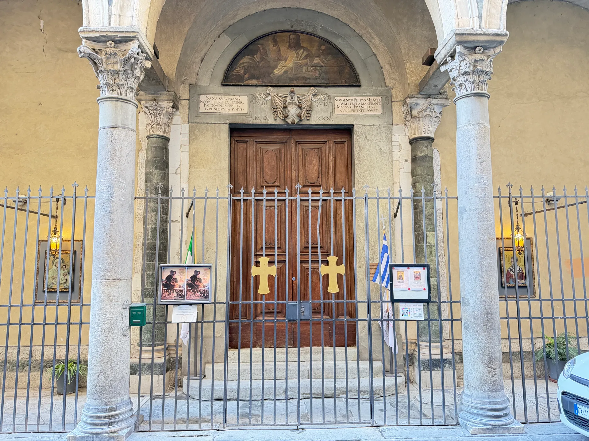 A church portico of paired stone columns behind an iron railing, the doors closed under a painted lunette.