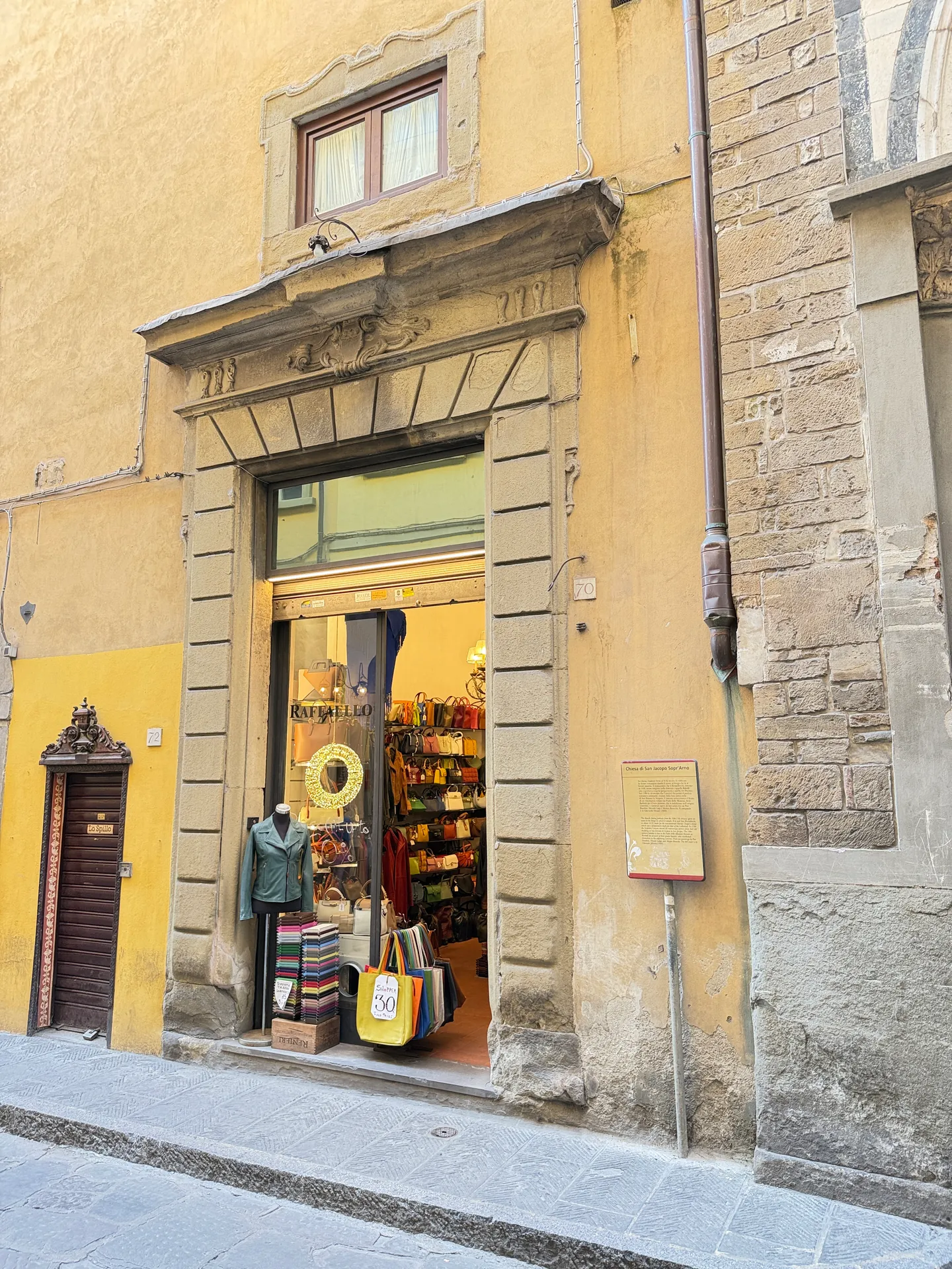 A leather shop with bags and belts hung in the doorway and set out on the pavement.