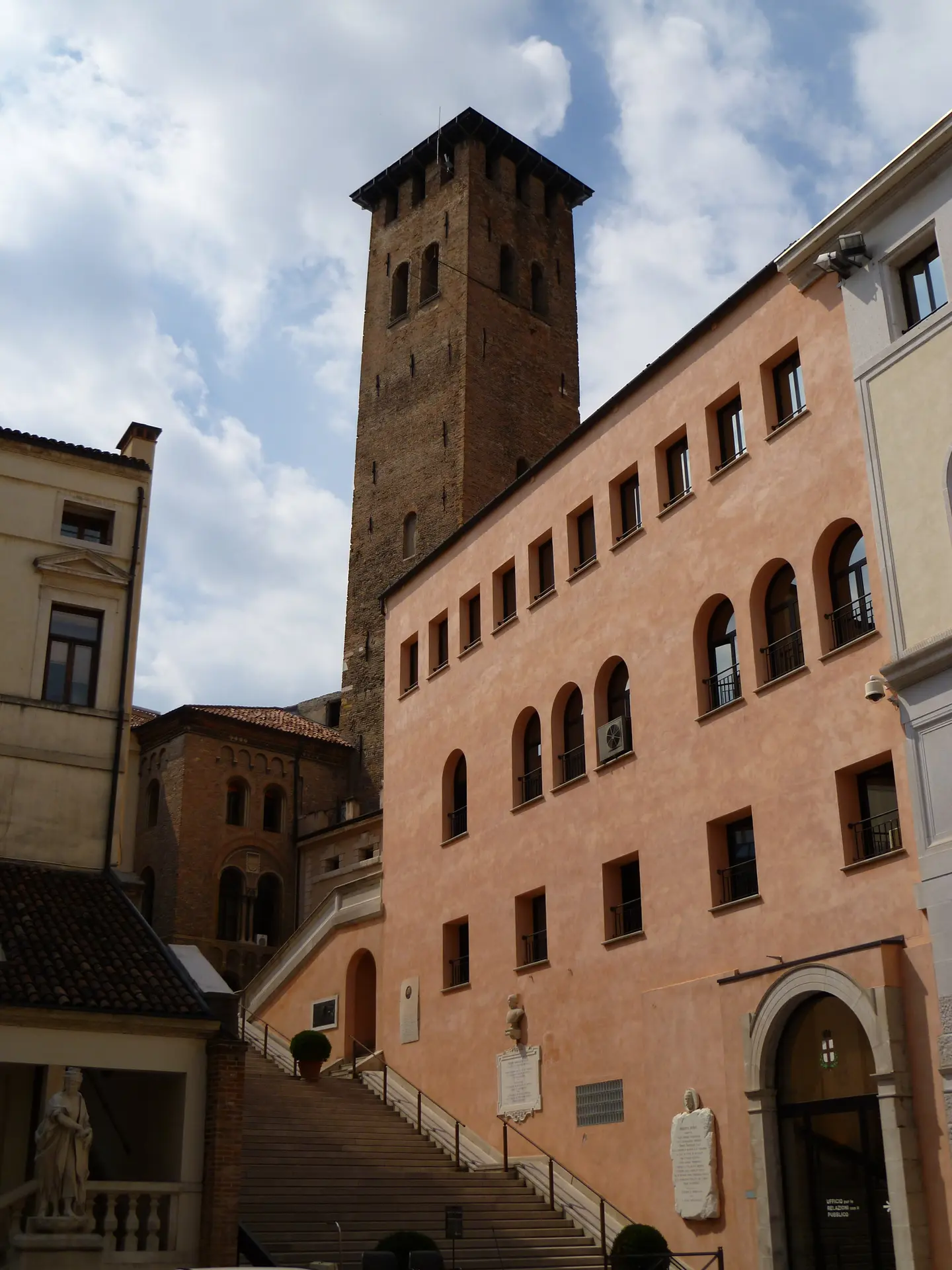 A medieval brick tower rising behind a pink palazzo with a broad external staircase in Padua