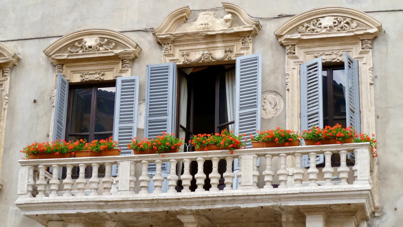A Baroque balcony in Verona planted with red geraniums below shuttered windows