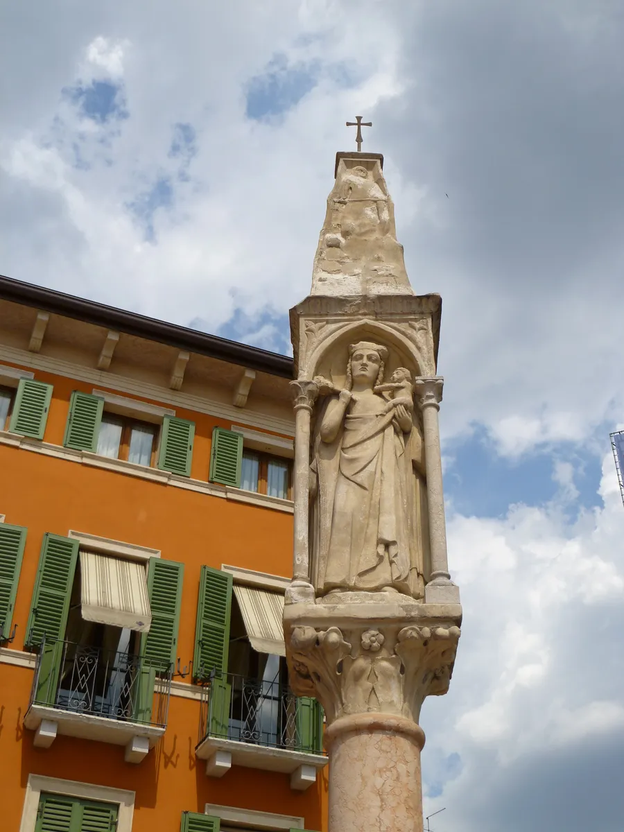 A carved saint standing under a Gothic canopy on a column in Verona