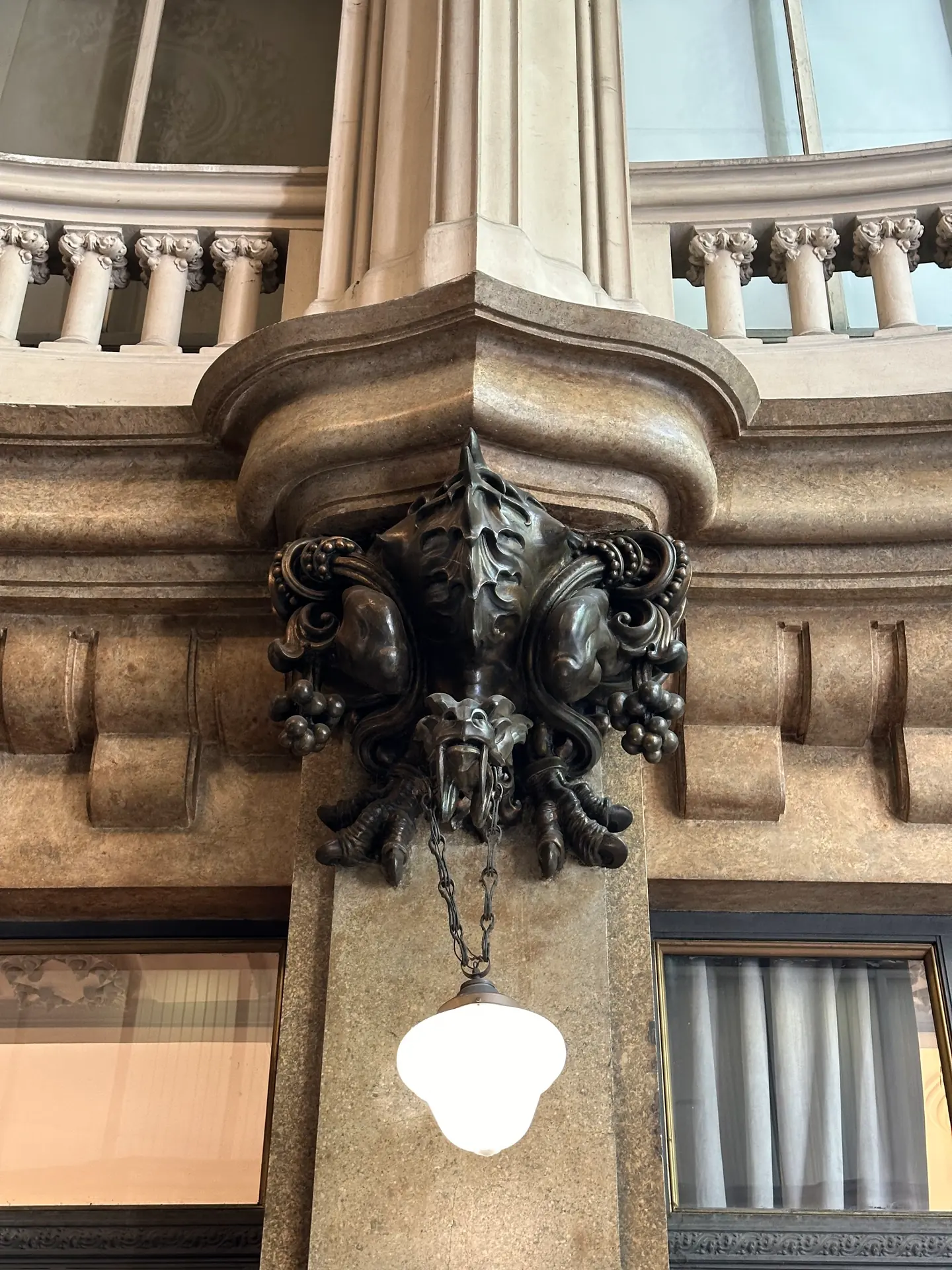 A bronze creature corbel carrying a lamp beneath a stone cornice in the Barolo lobby.