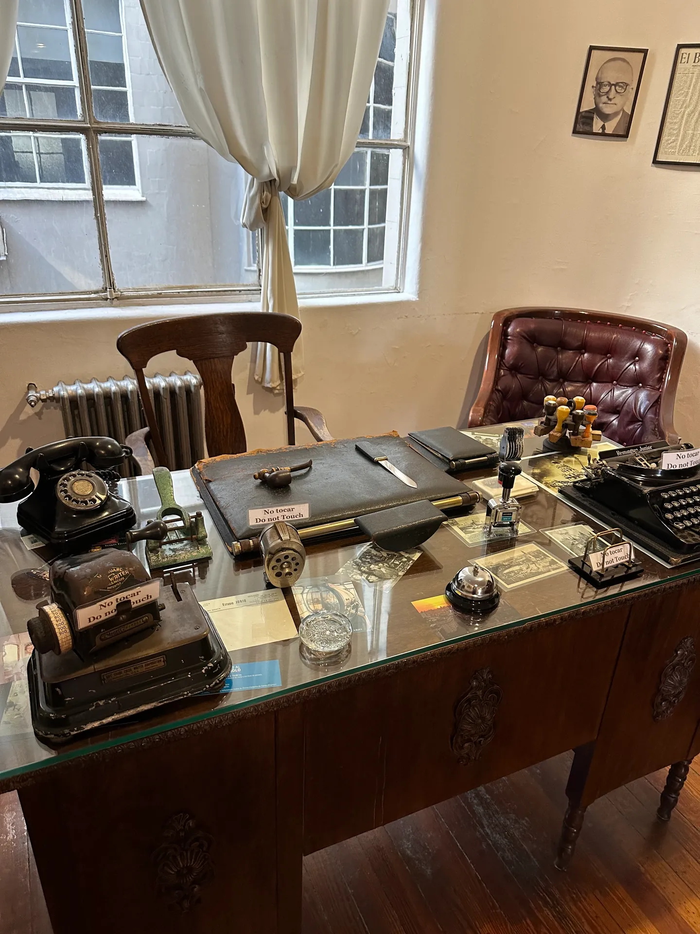 A period office desk with a black telephone, typewriter and blotter in window light.
