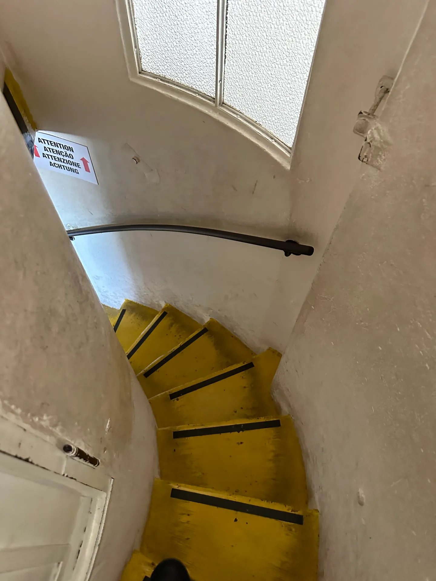 A tight spiral service staircase with yellow-painted step edges seen from above.