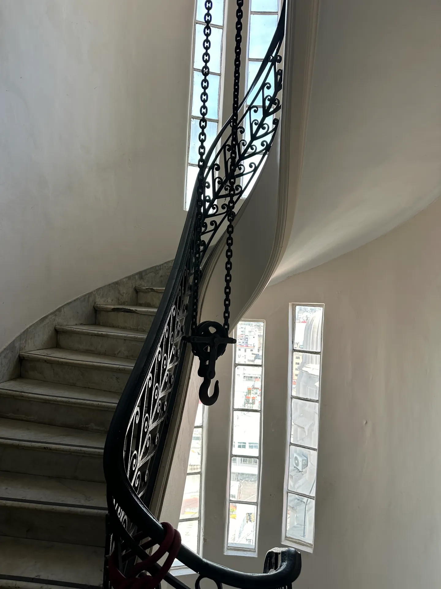 An ornamental spiral staircase with wrought-iron balustrades lit by side windows.