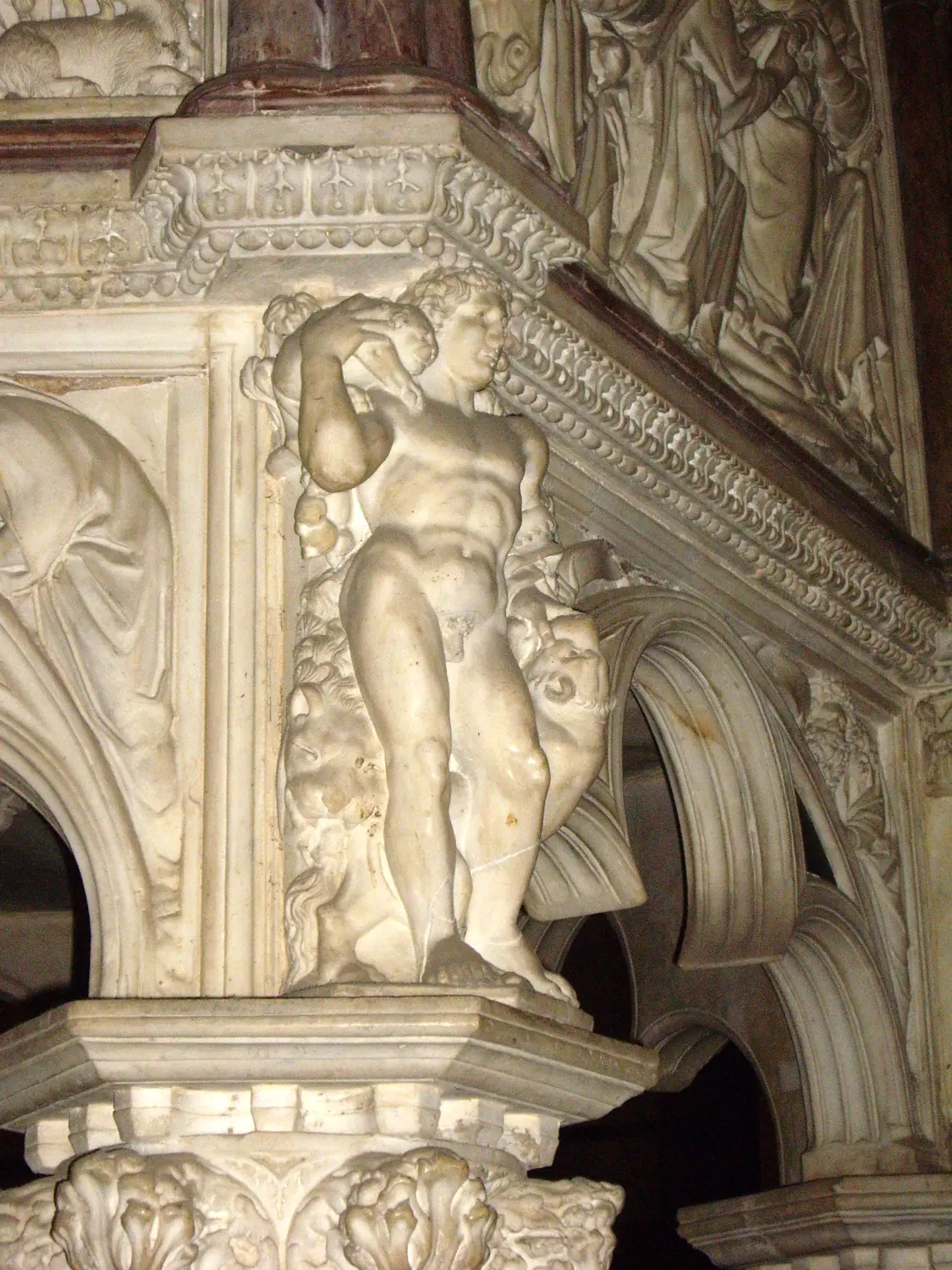 A carved marble figure crouching under a cornice inside Pisa cathedral