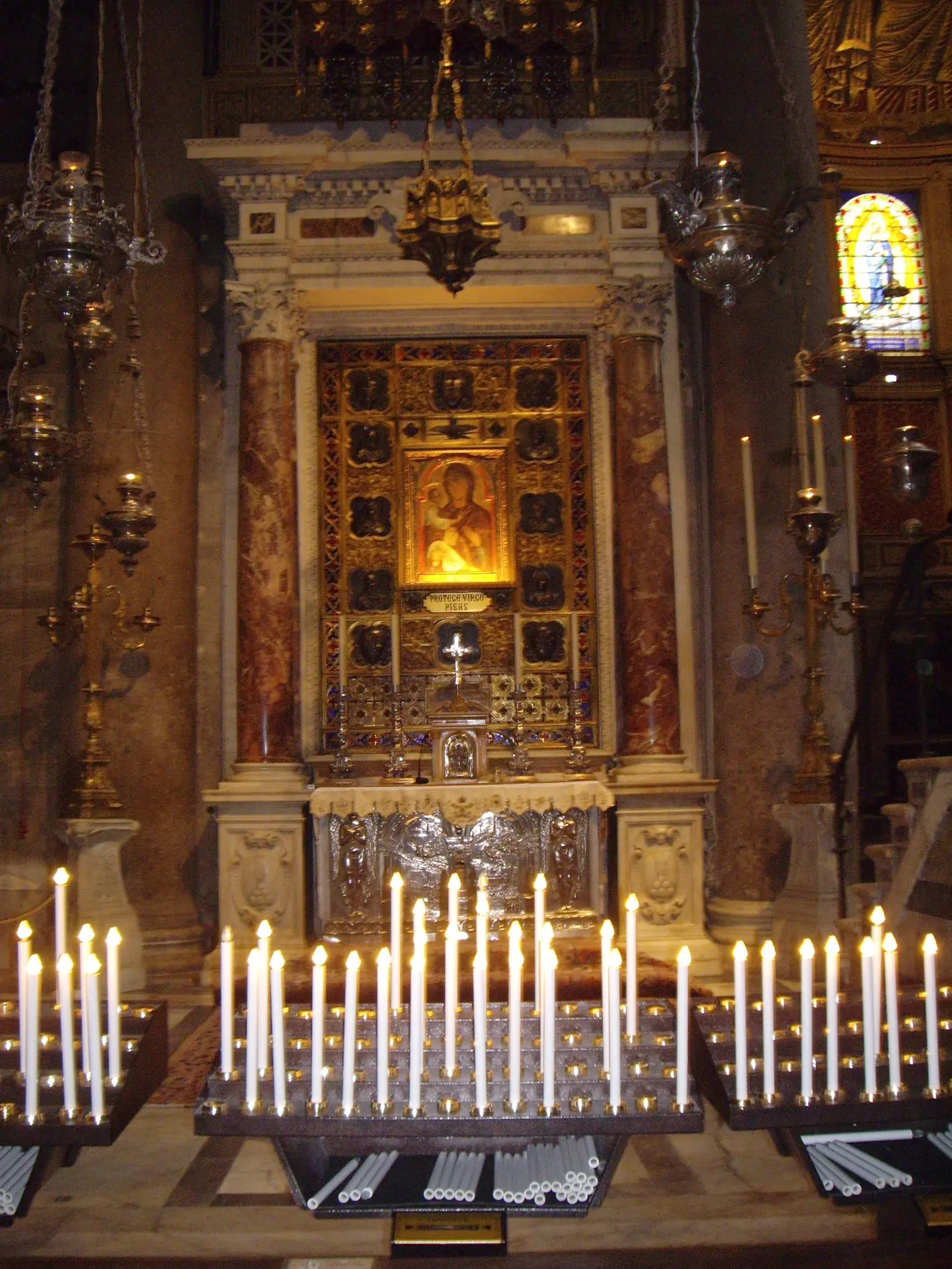 A rack of lit votive candles before a gilded side altar in Pisa cathedral