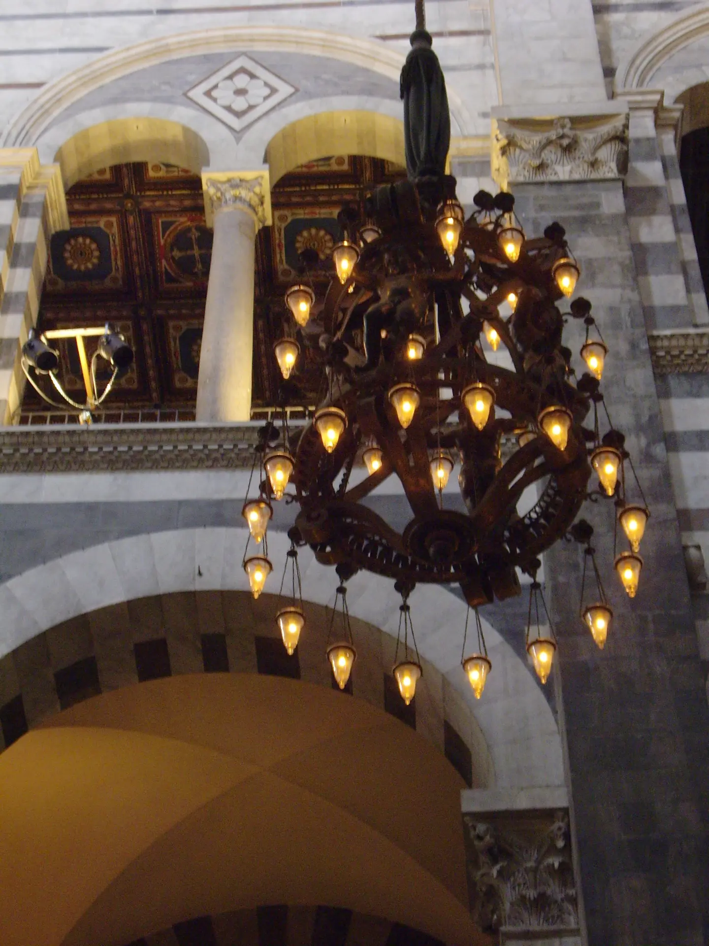 A wrought iron chandelier lit under the arcades of Pisa cathedral